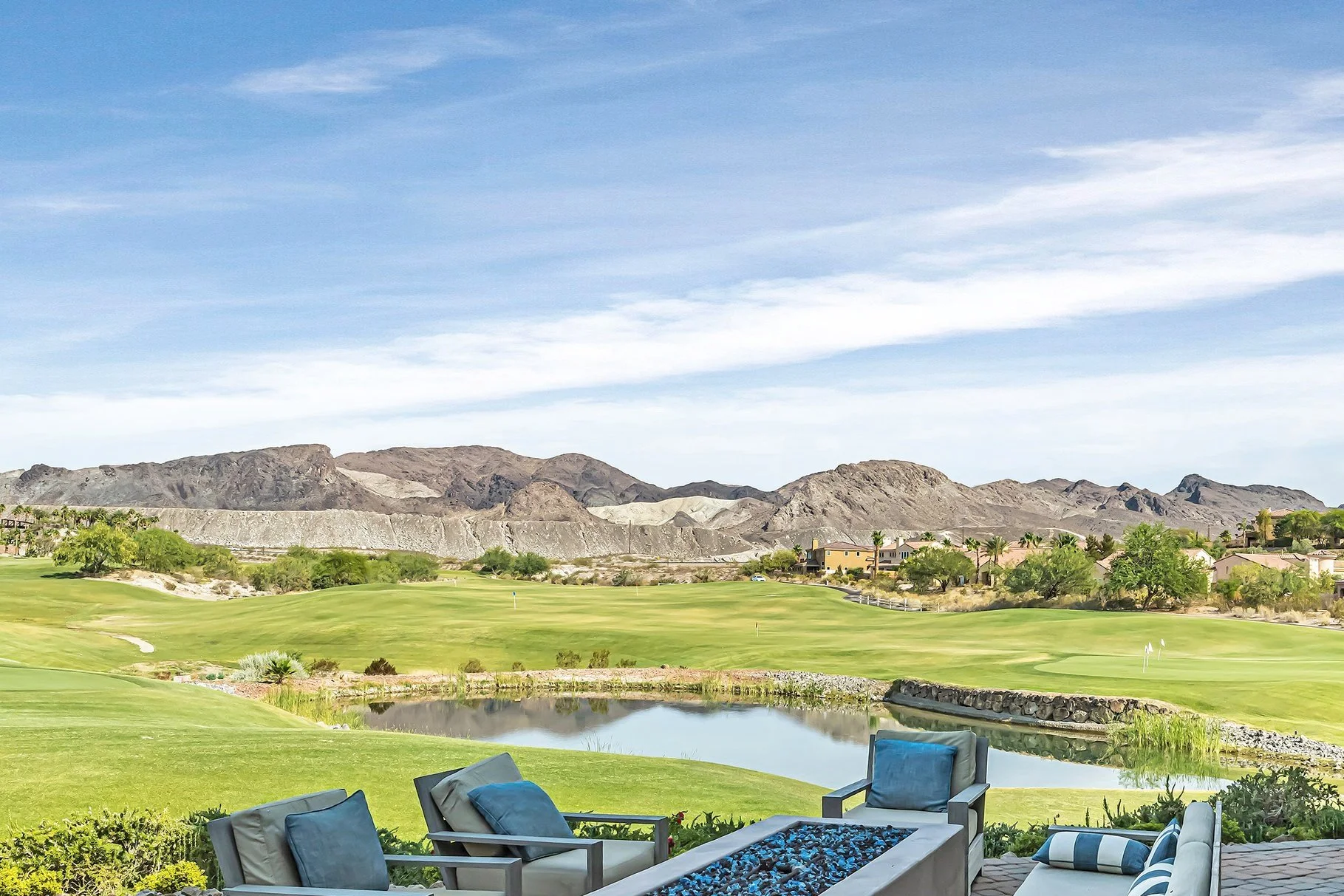 Lake Las Vegas Sports Club golf course with green fairways, driving range, pond, background mountain ranges.