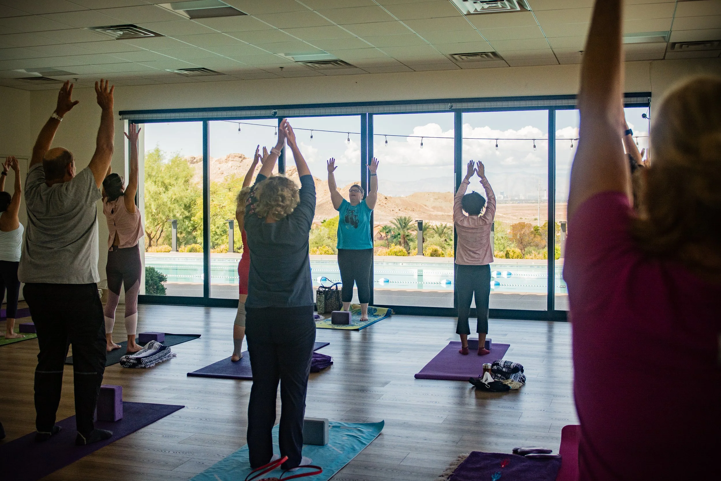 Lake Las Vegas Sport Club members practicing yoga in a studio with large windows overlooking a desert landscape.