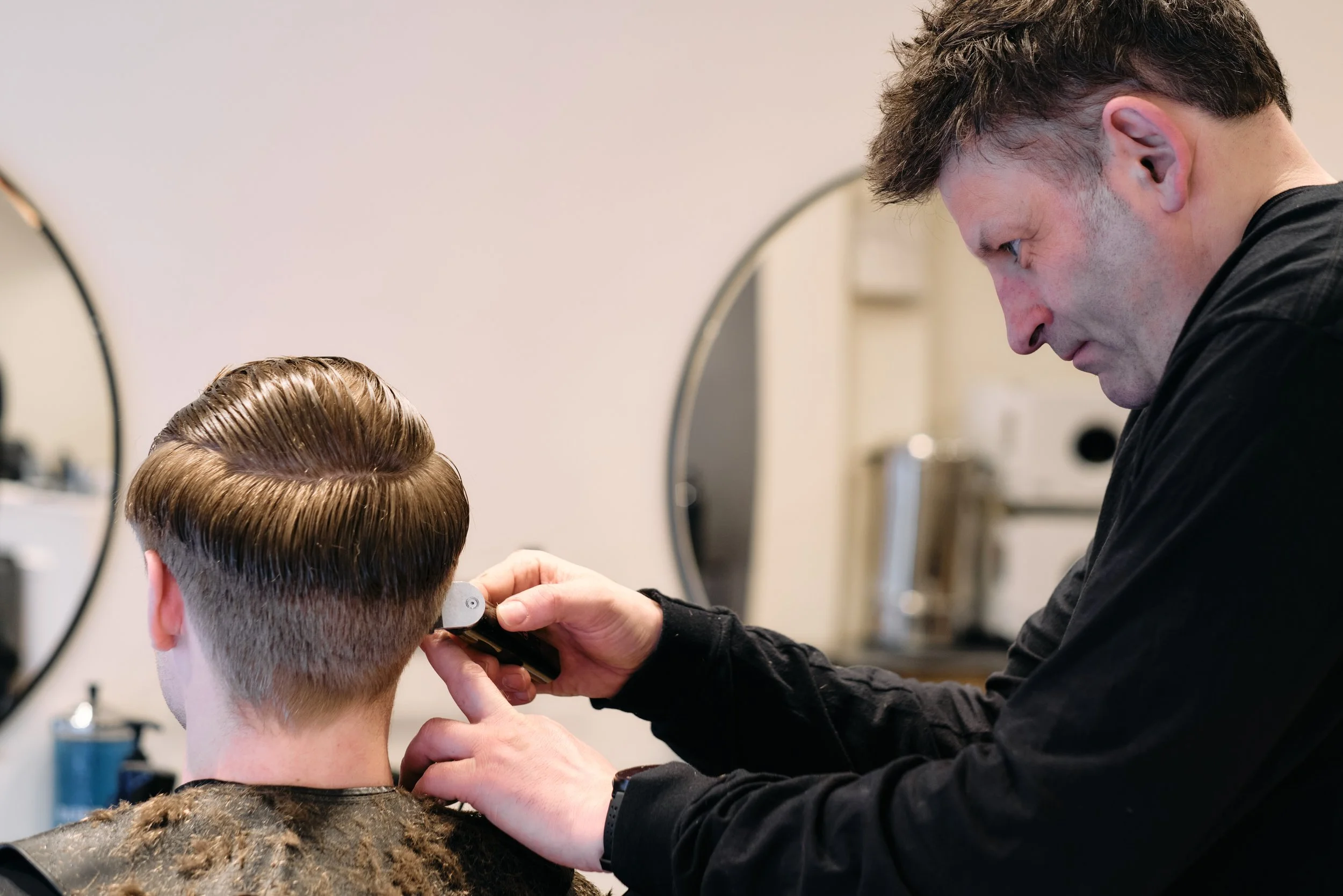 Barber gives a man a haircut with clippers in a salon.