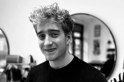 A young man with curly hair smiling in a mirror Reflection