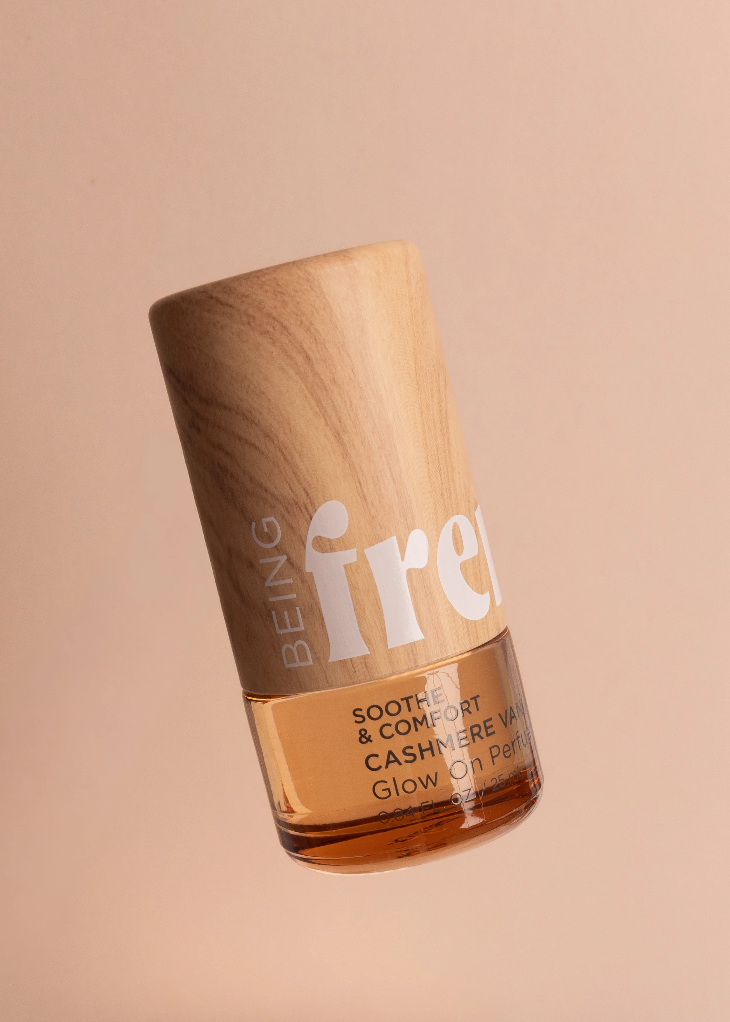 A bottle of Being French oil perfume floating on a salmon colored background