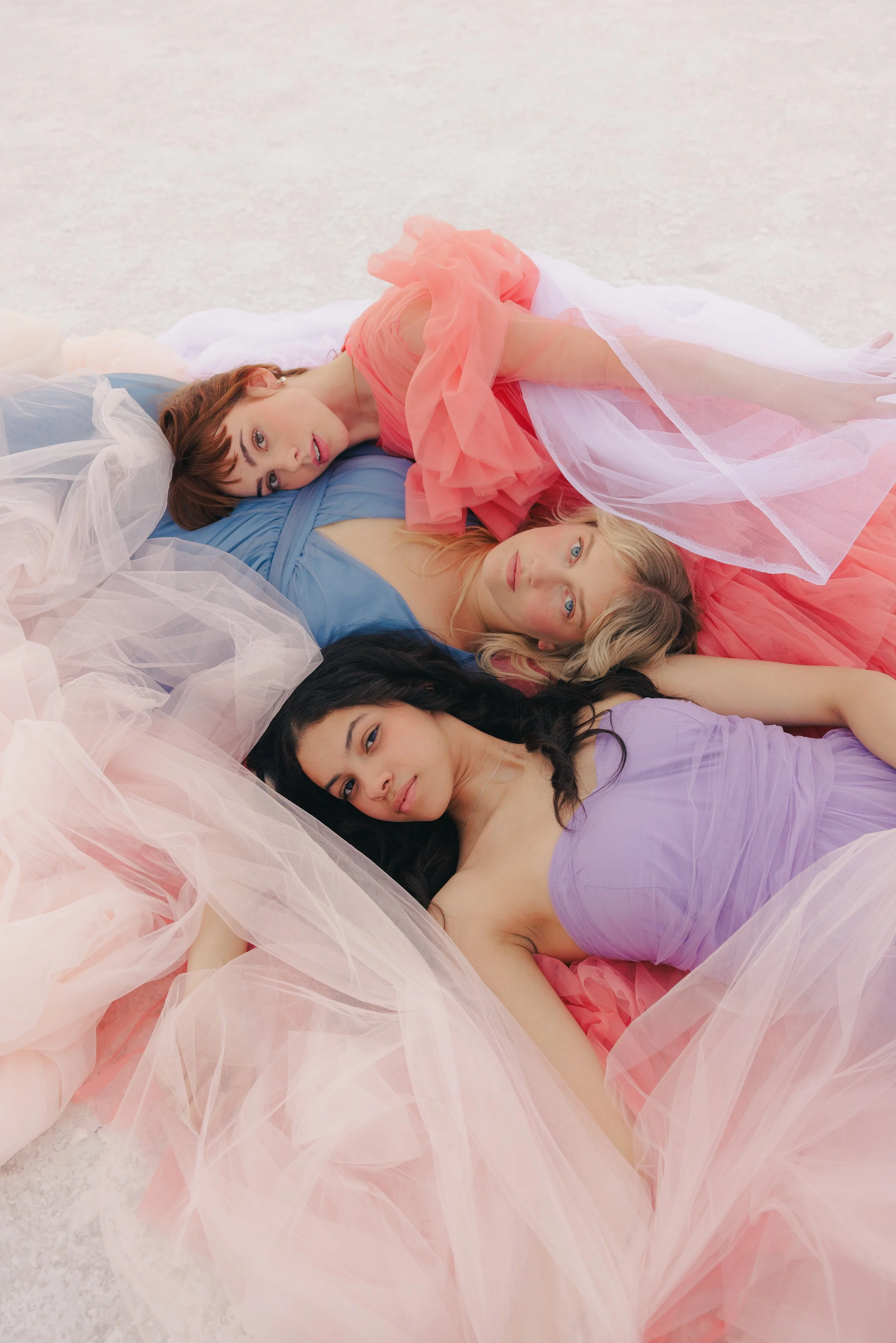Three women are laying together in the Salt Flats wearing pink, purple, and blue