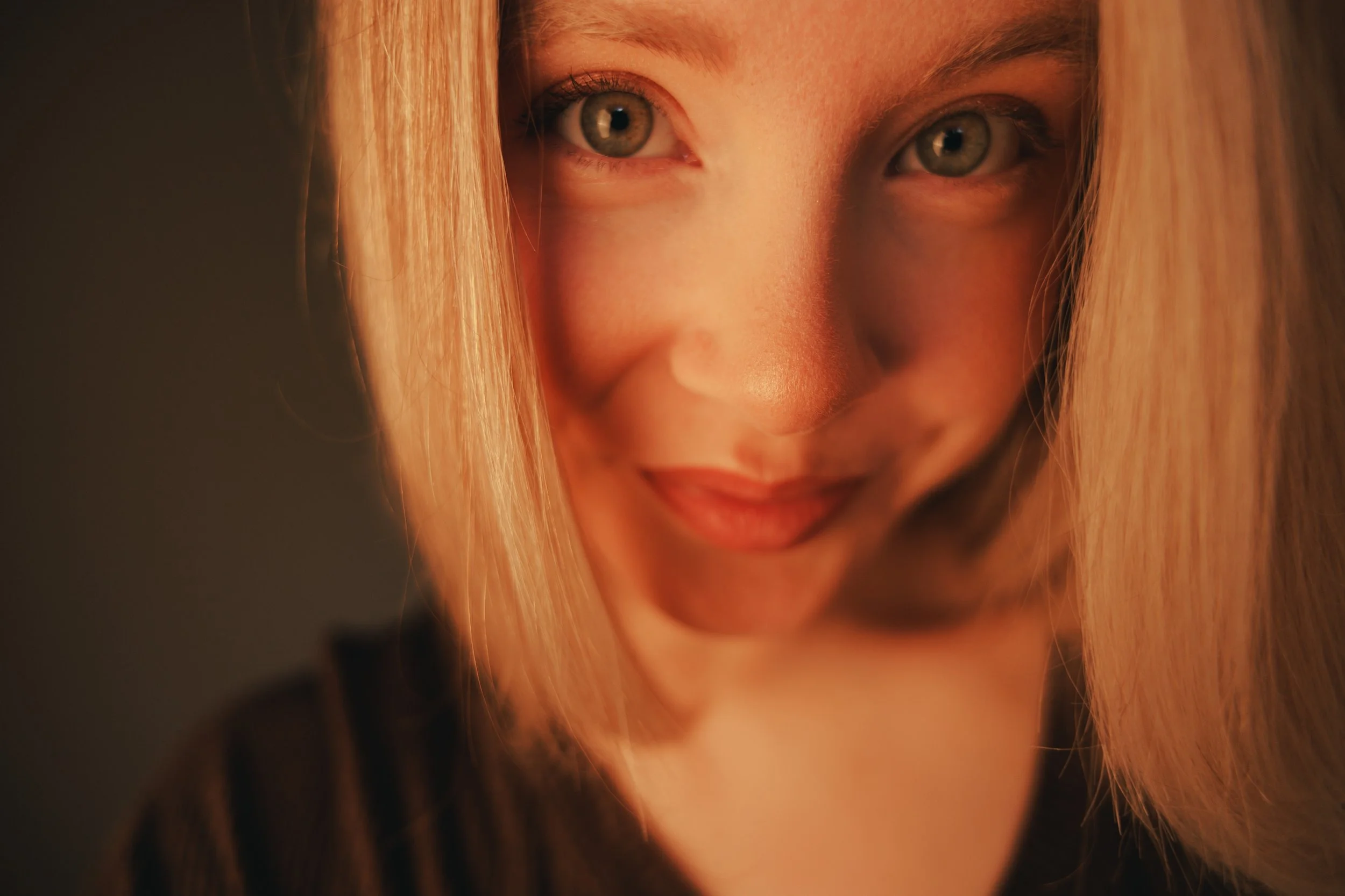 Close-up of a woman's face with blonde hair, green eyes, and a slight smile, looking to the side.