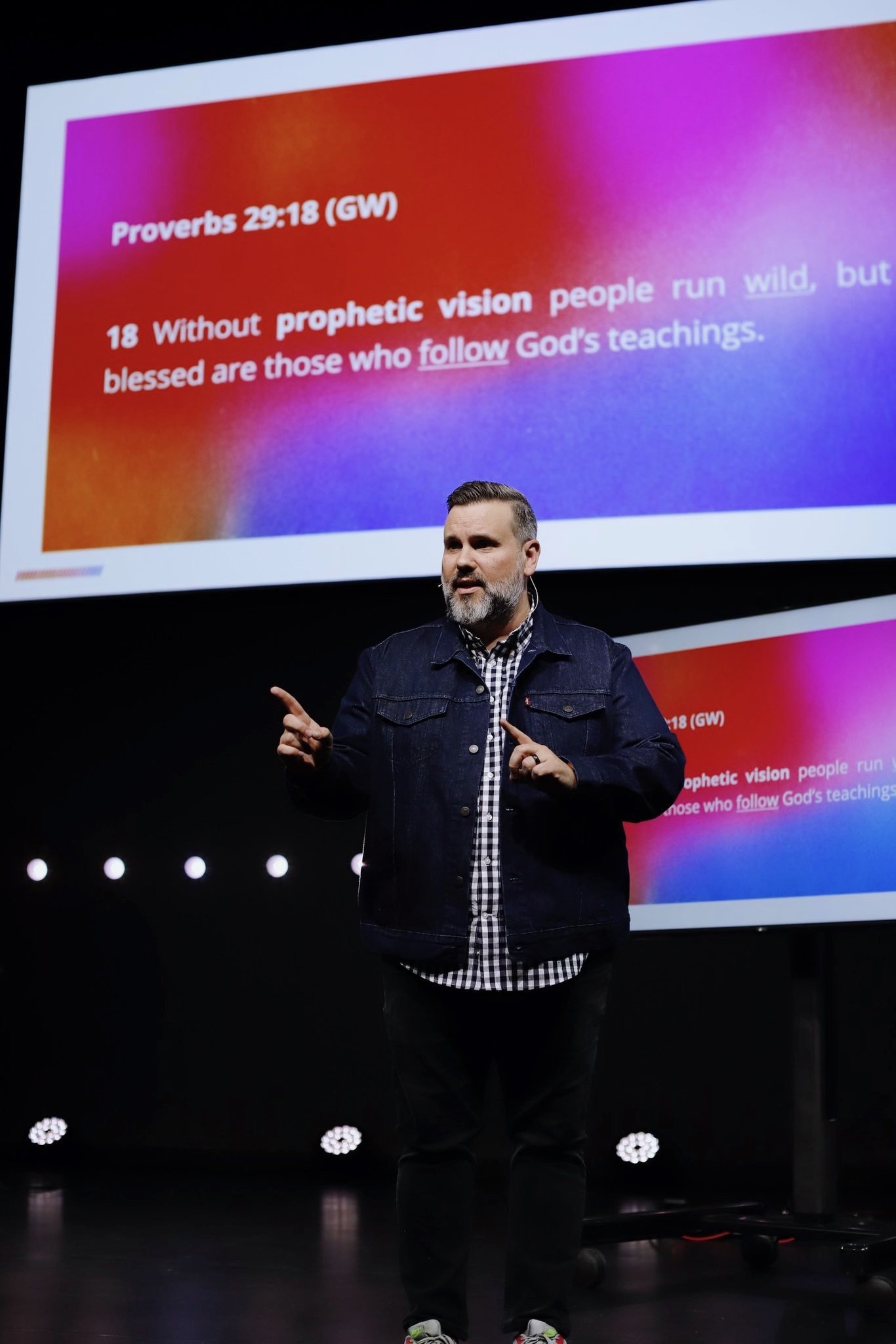 Portrait of a smiling man with a beard, wearing a denim jacket, against a blue background.