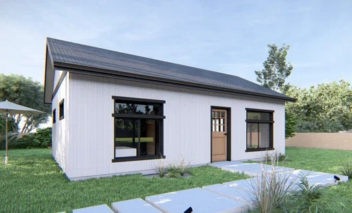 A small white house with black window frames and a brown door, situated in a grassy yard with a paved walkway and trees in the background.