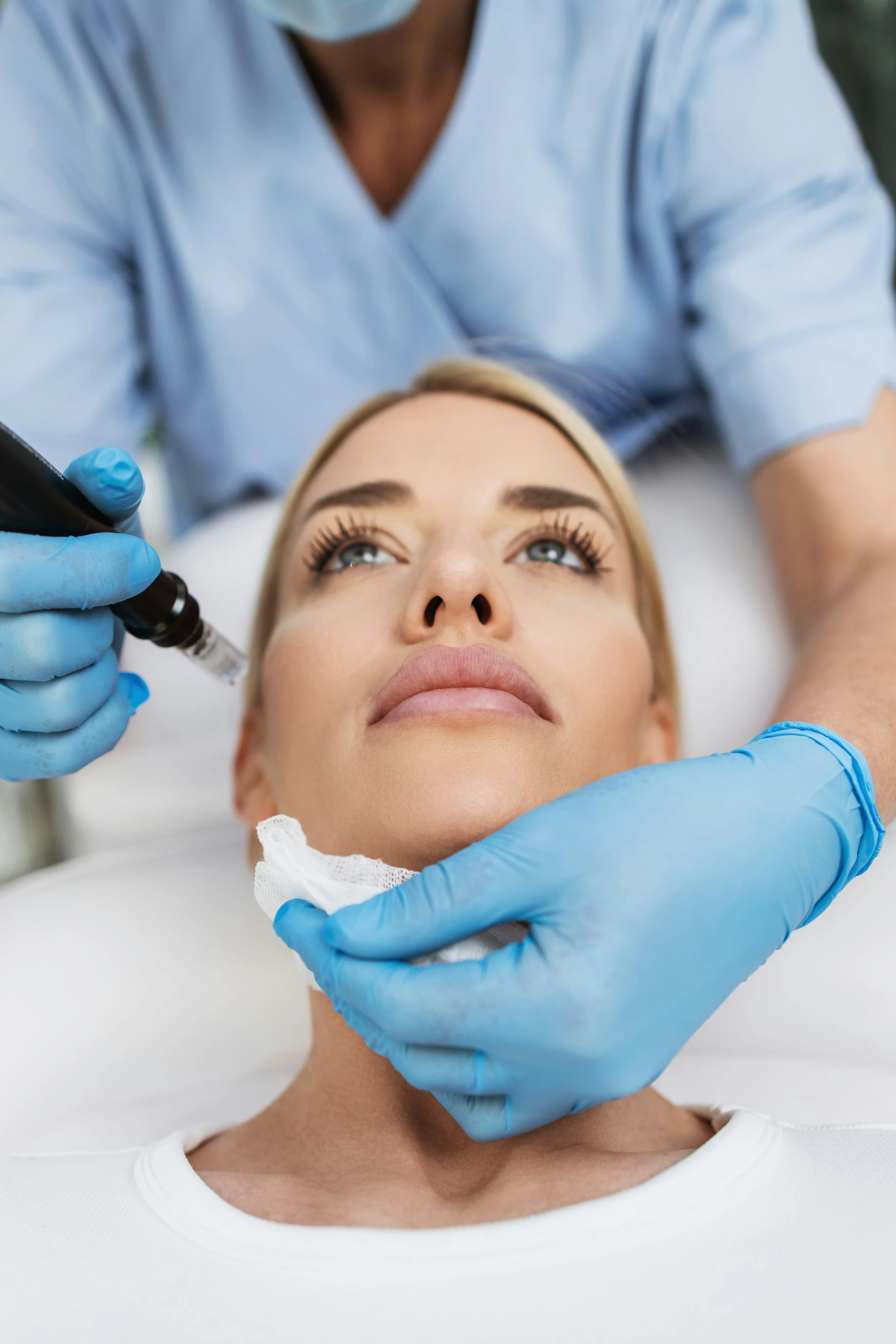 A woman laying down at a treatment table getting a facial treatment done.