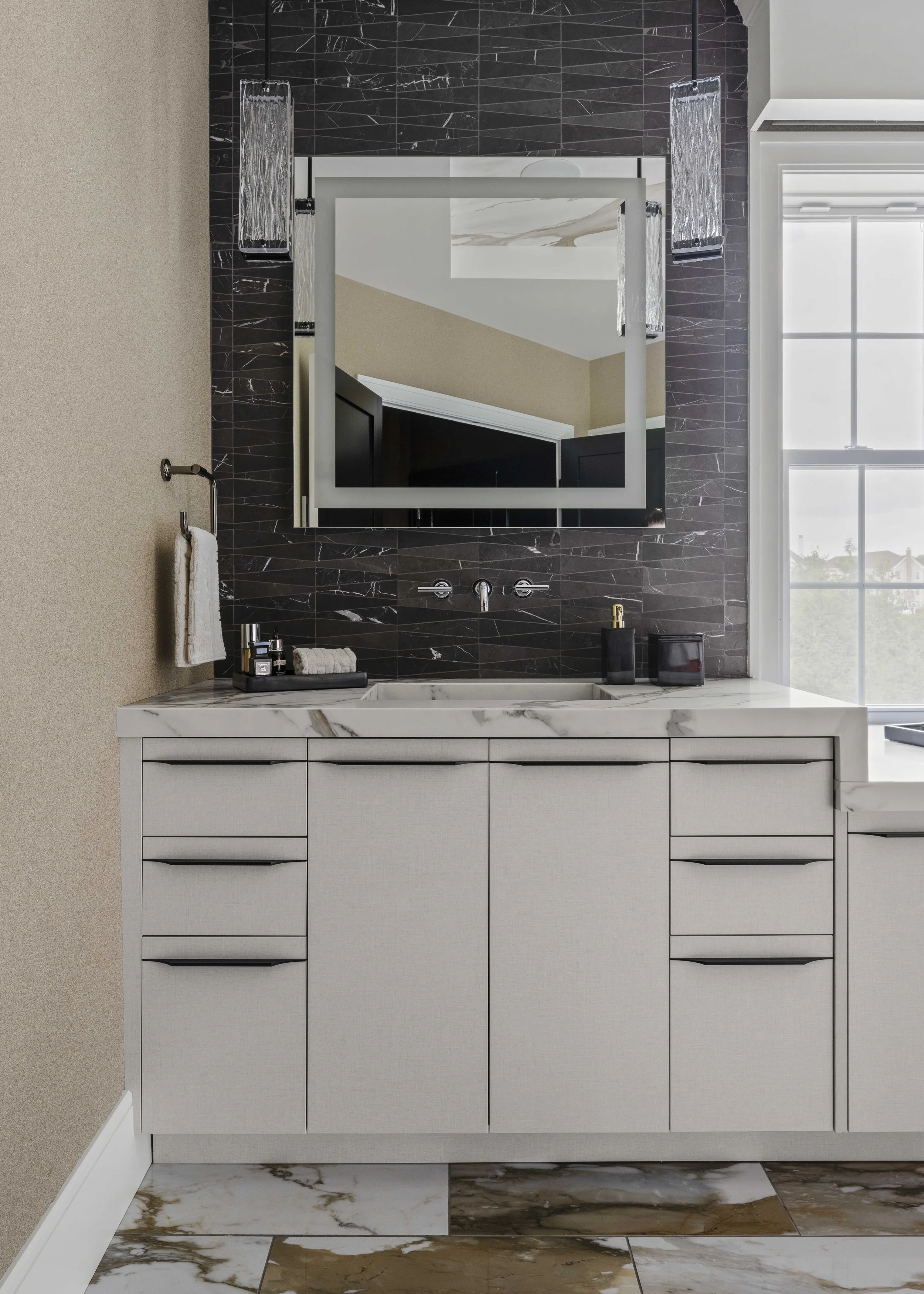 A modern bathroom sink area featuring a backlit square mirror, black textured tile backsplash, and a white marble countertop.