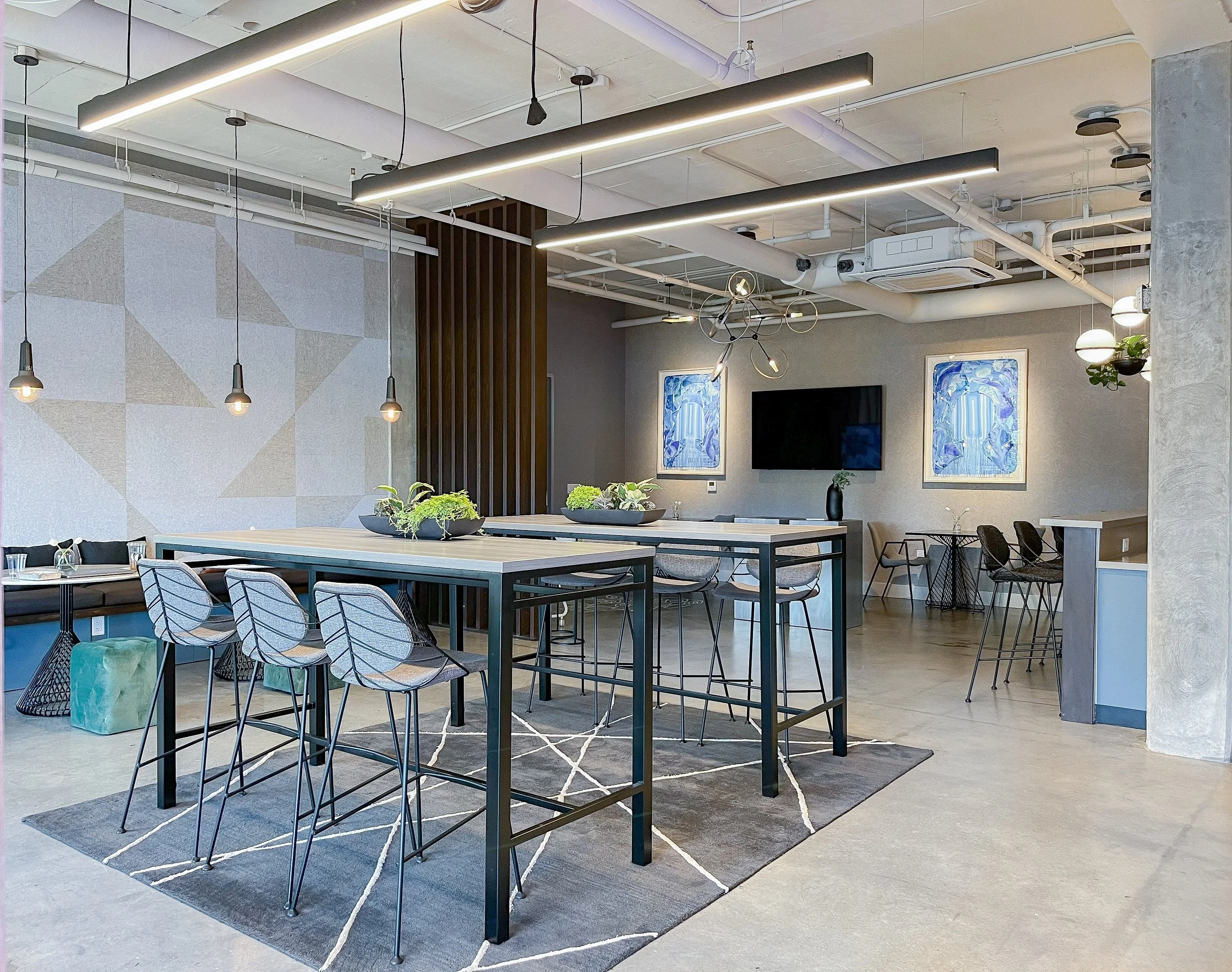 Black vertically-fluted island with six black counter stools, white subway tile backsplash with open shelving, sculptural black circular chandelier with LED rings, exposed ceiling with concrete beams, sphere pendant lights, blue framed artwork, polis