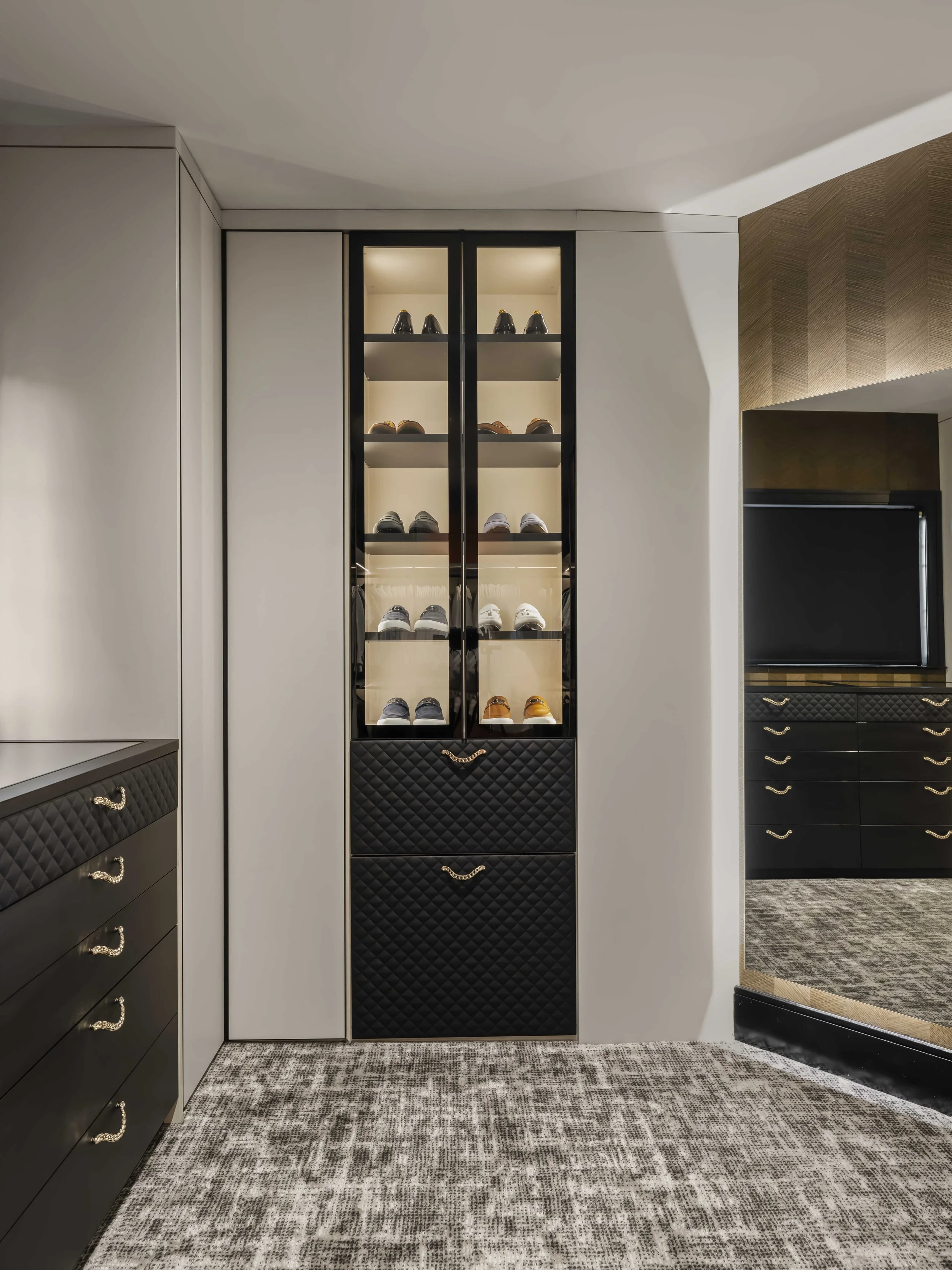 A floor-to-ceiling custom shoe cabinet with glass doors and internal lighting, positioned next to a large mirror in a modern dressing room