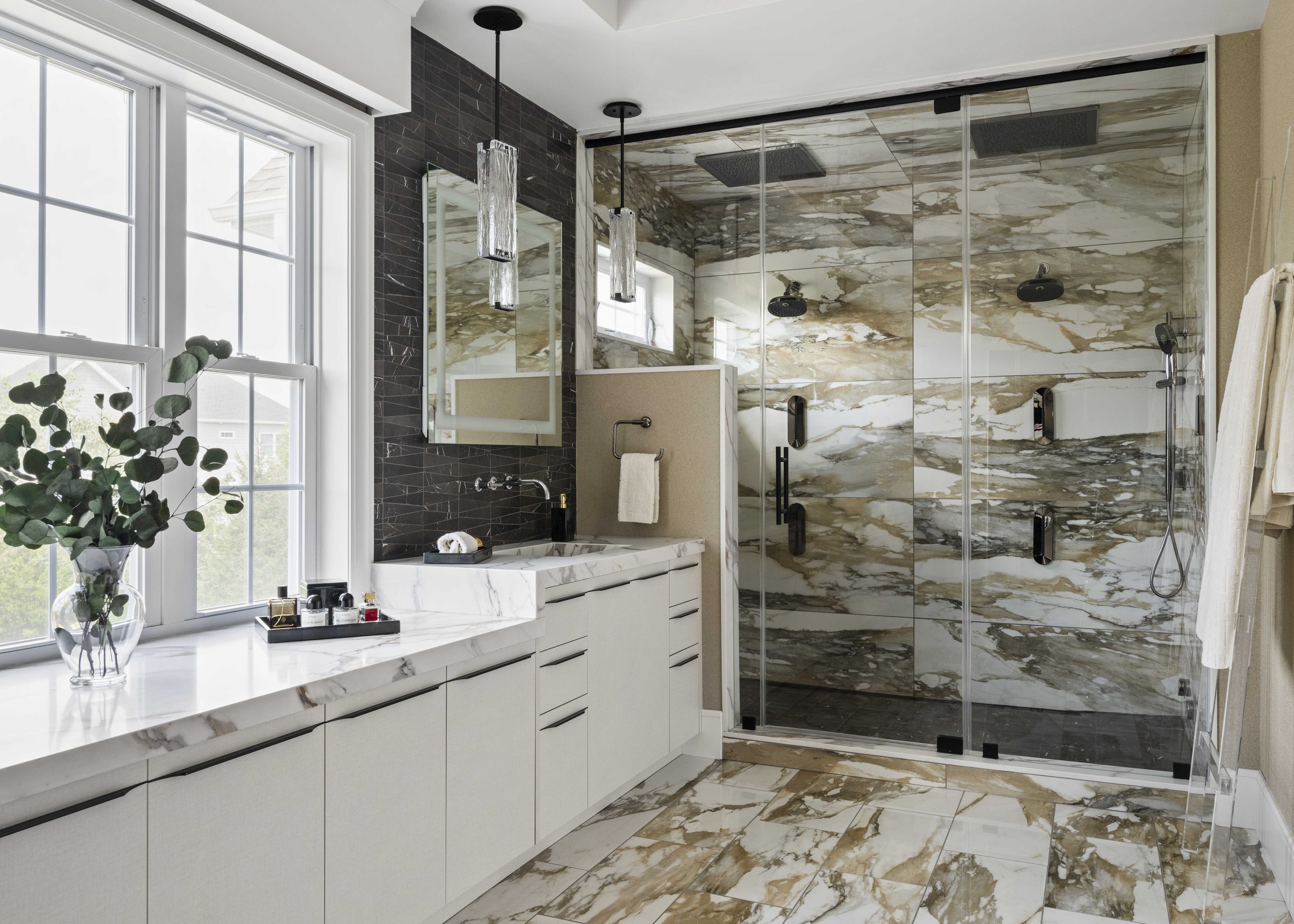 A luxury bathroom featuring a large walk-in shower with gold-veined marble tiles, a white marble vanity, and dark slate-style backsplash.