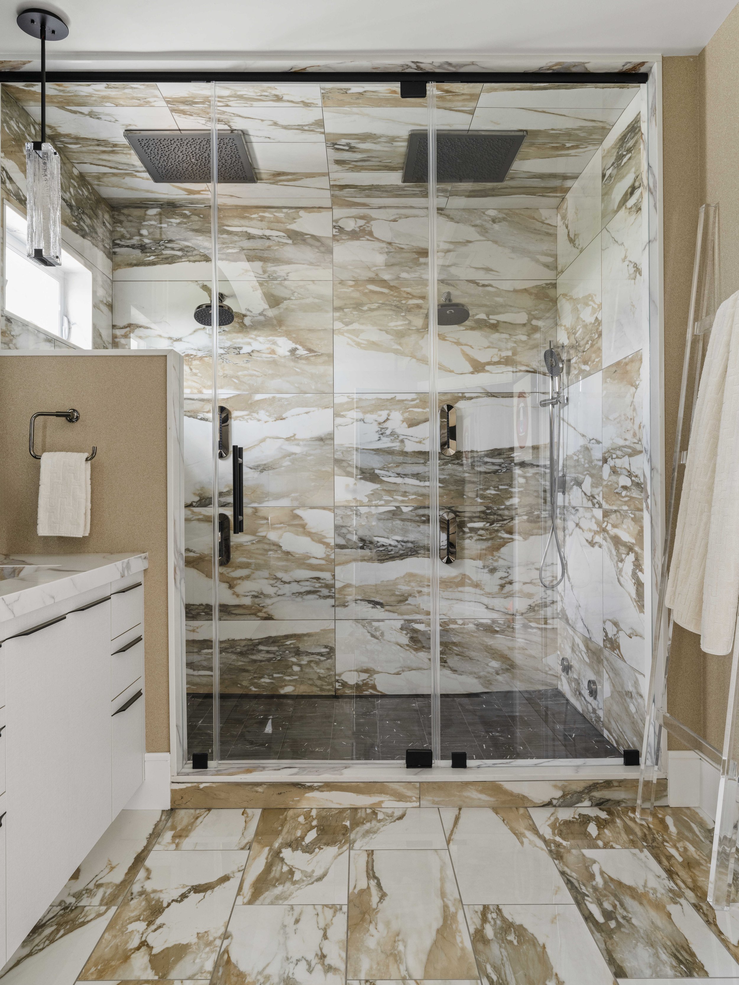 A spacious walk-in shower with dual rainfall showerheads and floor-to-ceiling white and gold marble tiles.