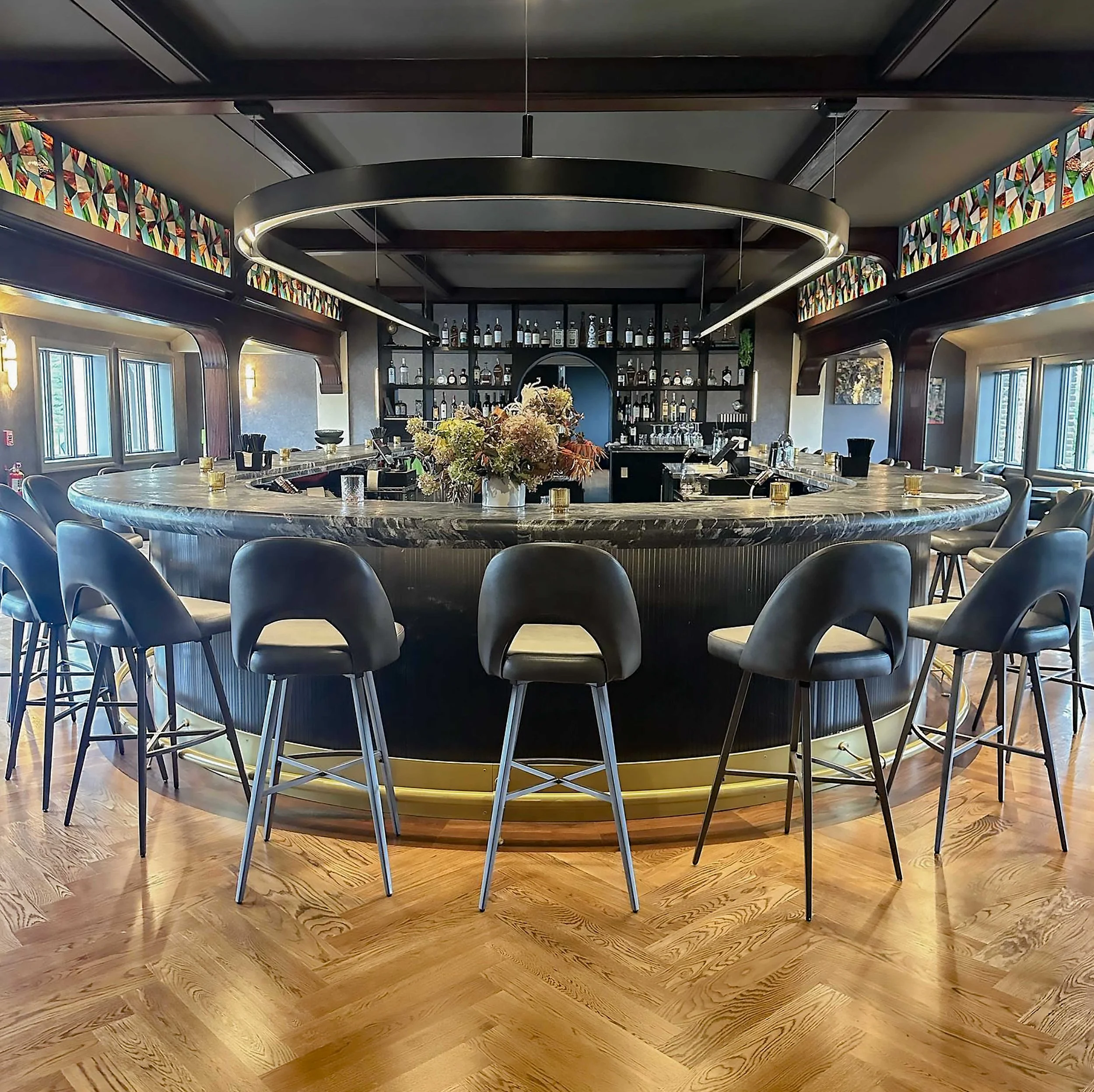 Close-up of a curved bar with a thick, grey veined marble top. In the background, a dark wooden architectural arch features a colorful stained-glass inlay above floral arrangements.