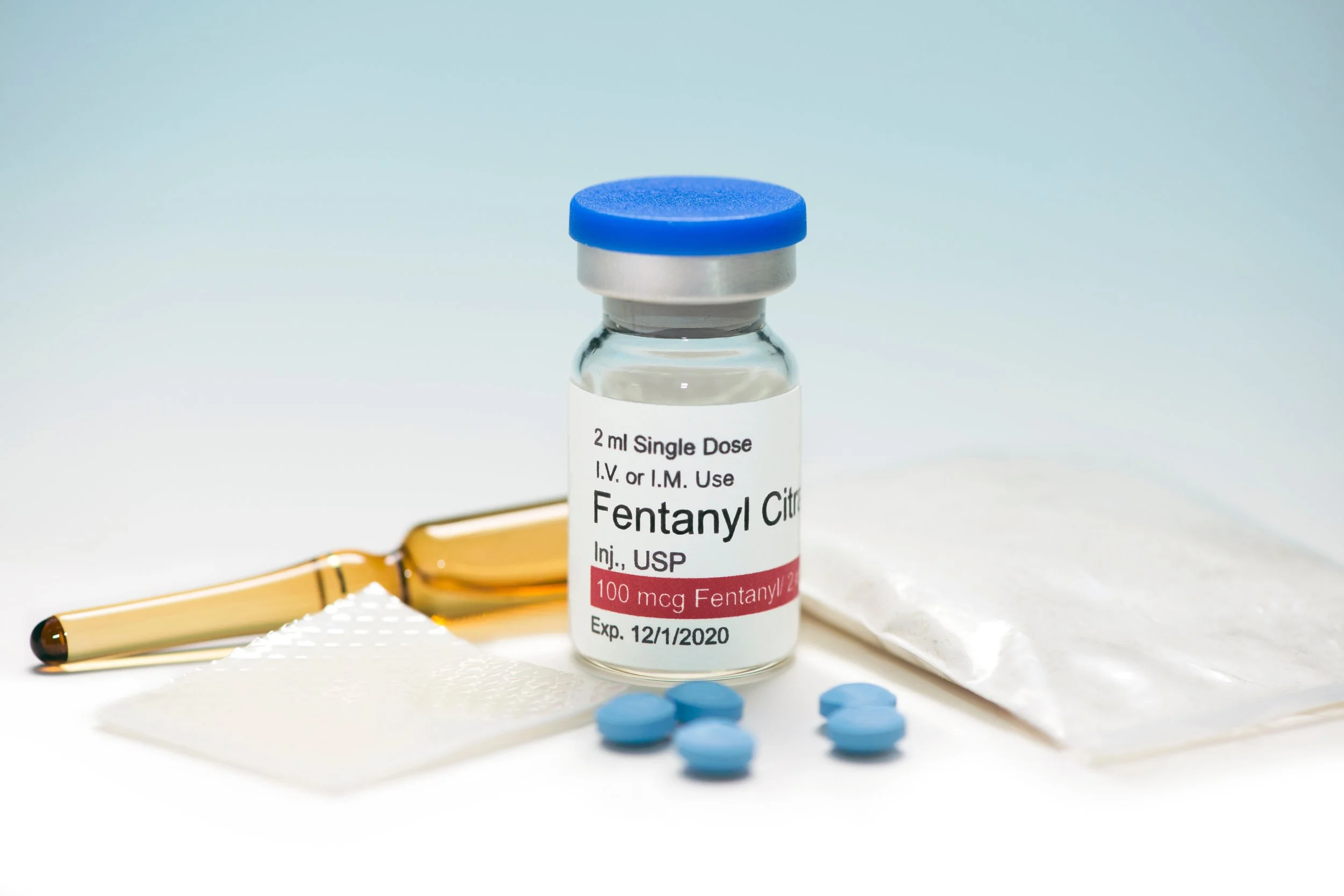 A vial of Fentanyl Citrate medication, blue pills, a blister pack, an ampoule, and a packet of powder are displayed on a white surface. Fighting fentanyl is a priority for Edward Jenkins for Lake County, Indiana Sheriff.