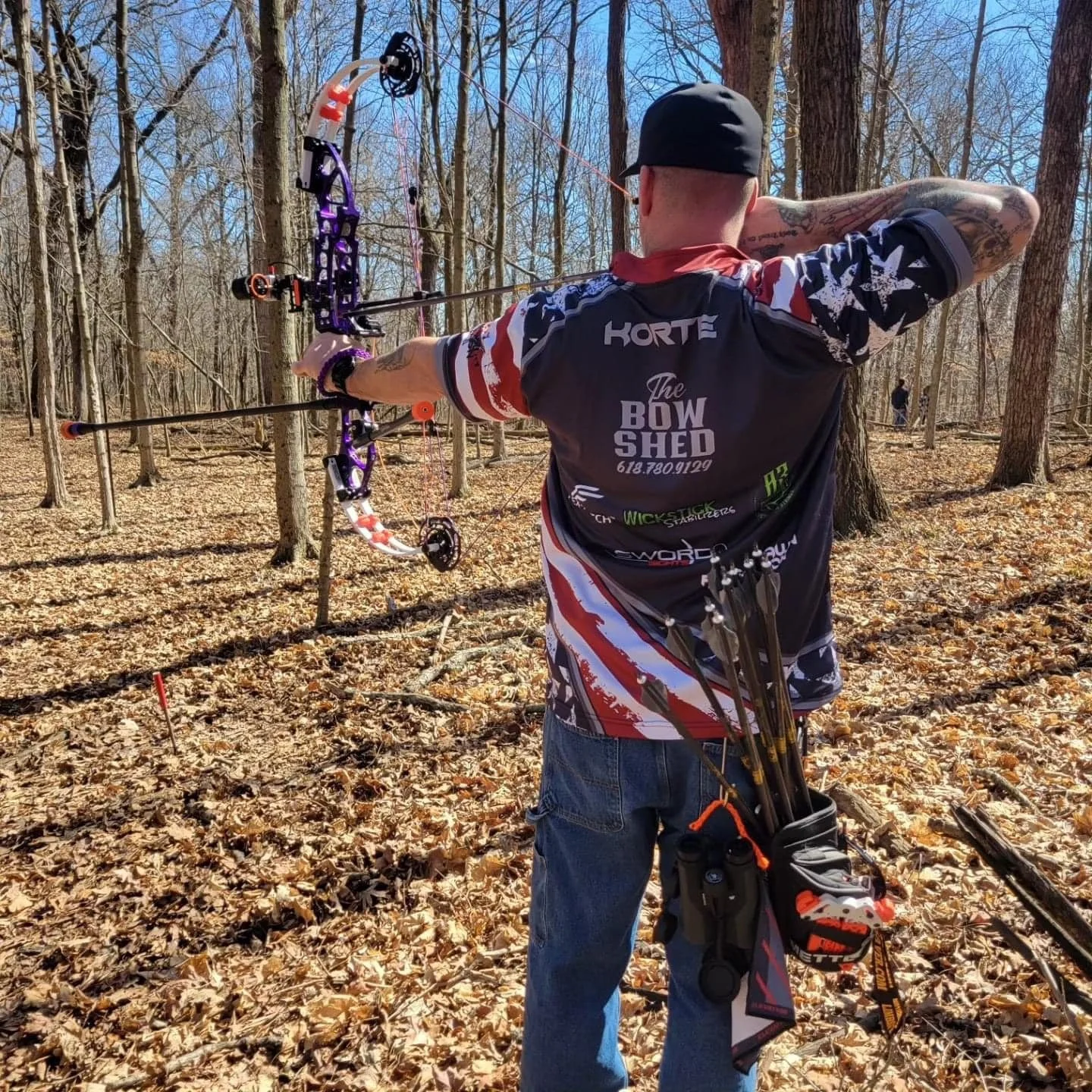 A man practicing archery in a wooded area, aiming a bow and arrow.