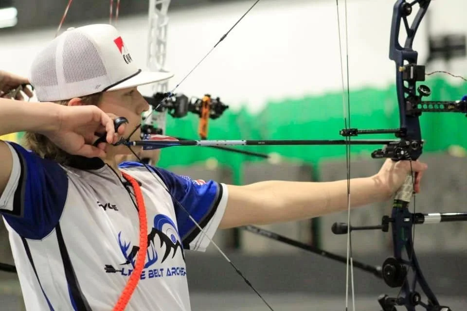 A female archer prepares to shoot an arrow at a practice or competition, focusing on her target with her bow drawn.