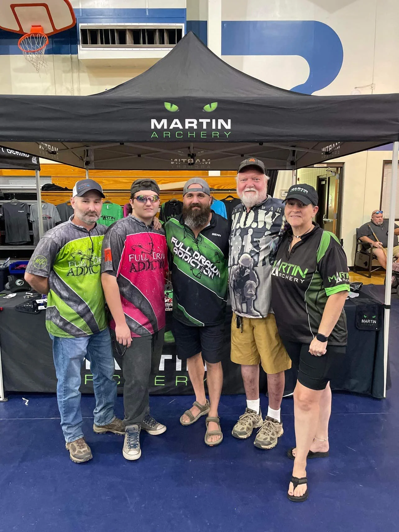 Group of five people standing inside a sports store in front of a tent and merchandise, with a basketball hoop visible in the background.