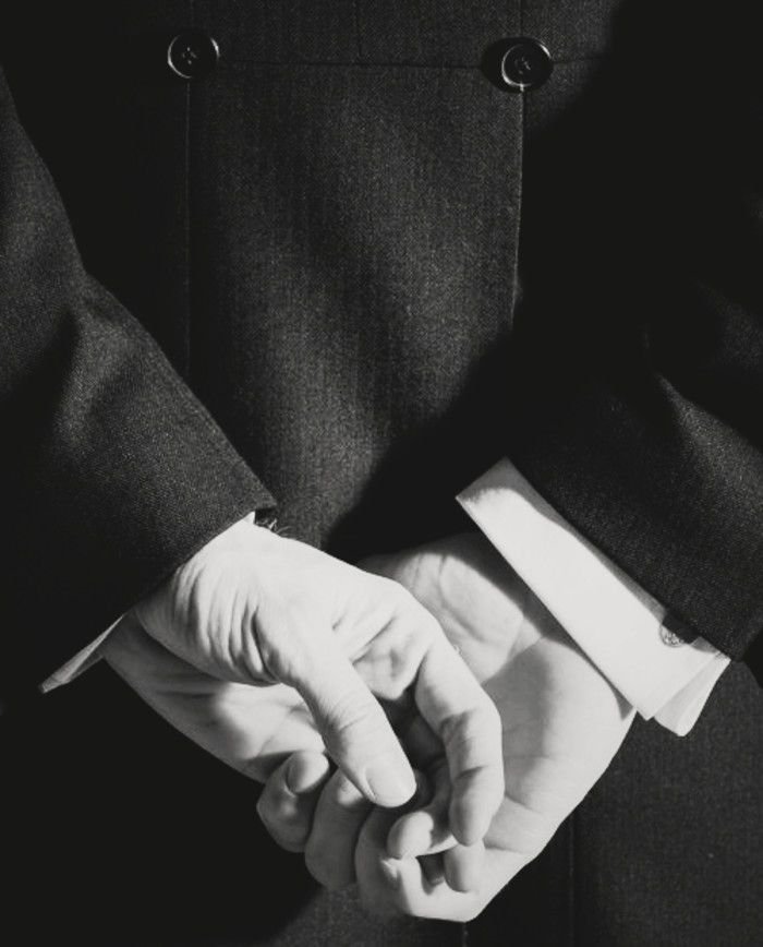 Two people in suits holding hands, close-up of their clasped hands with a focus on their fingers.
