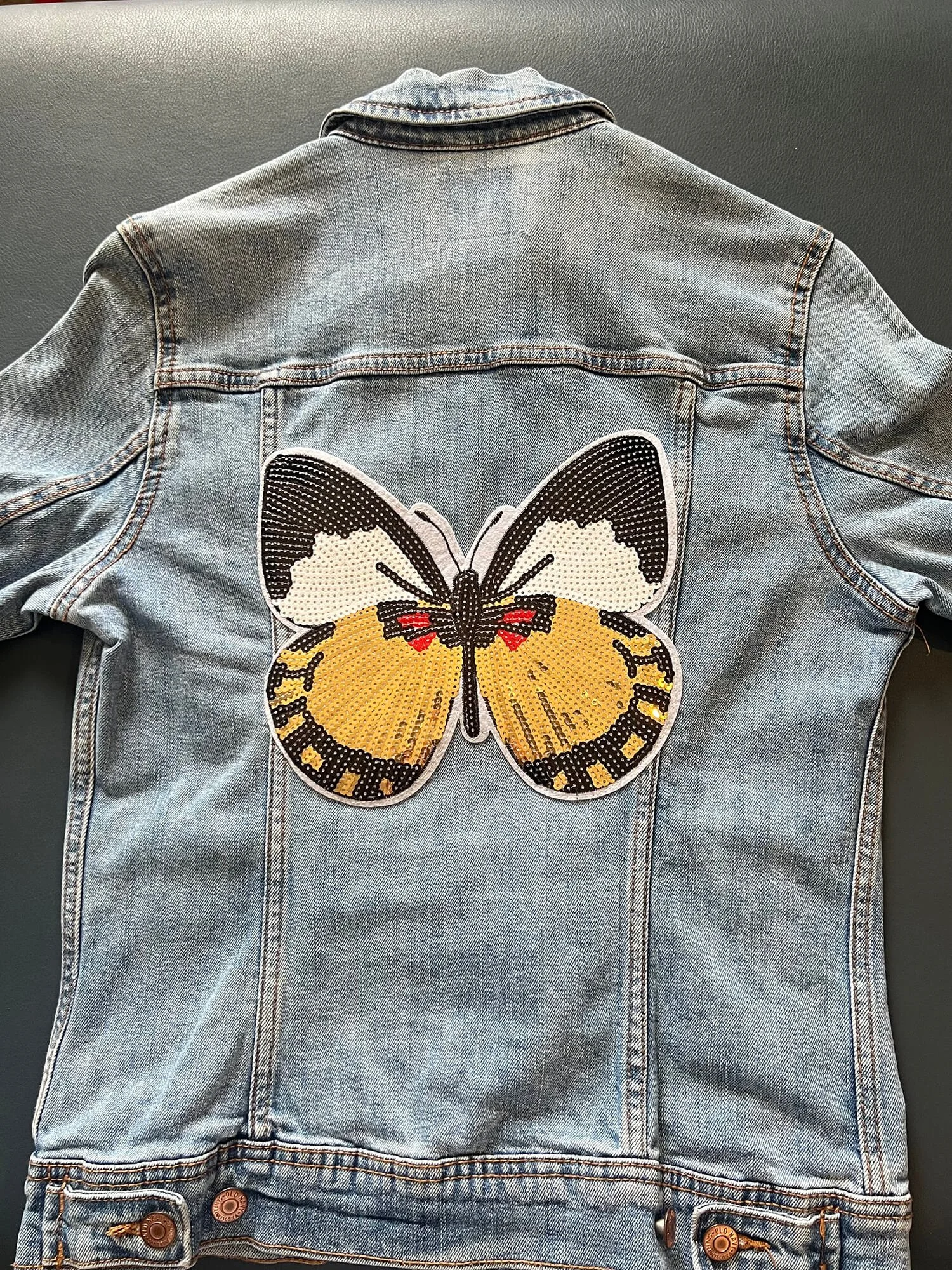 Back of a denim jacket with a large butterfly patch embroidered on the back.