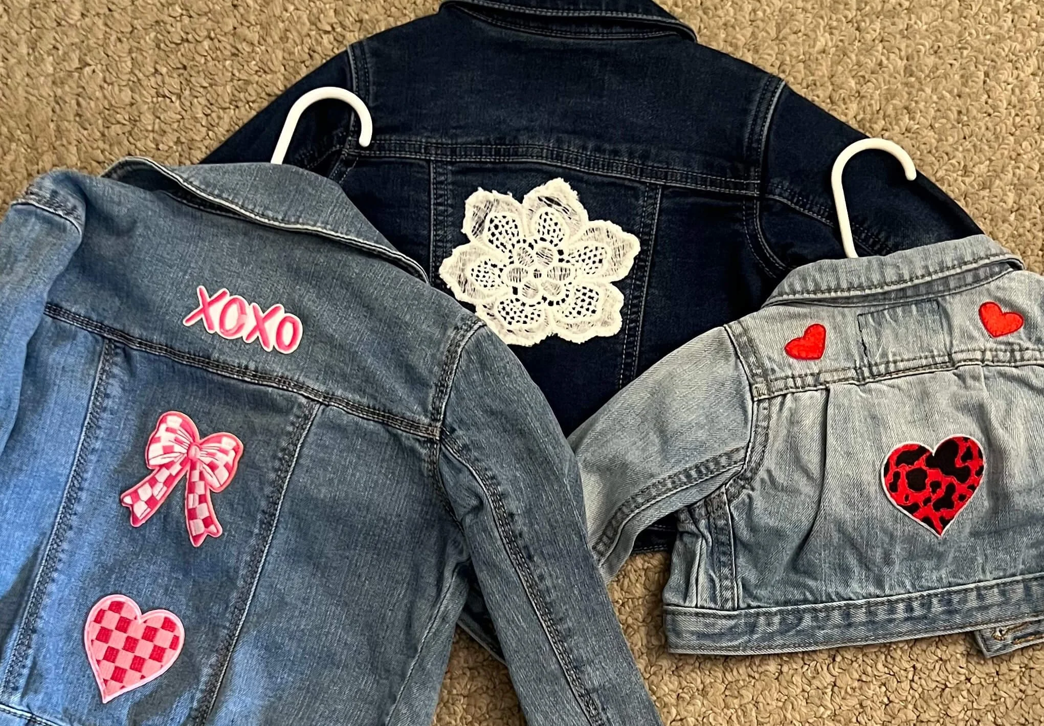 Three denim jackets with heart and bow patches laid on a carpeted floor.
