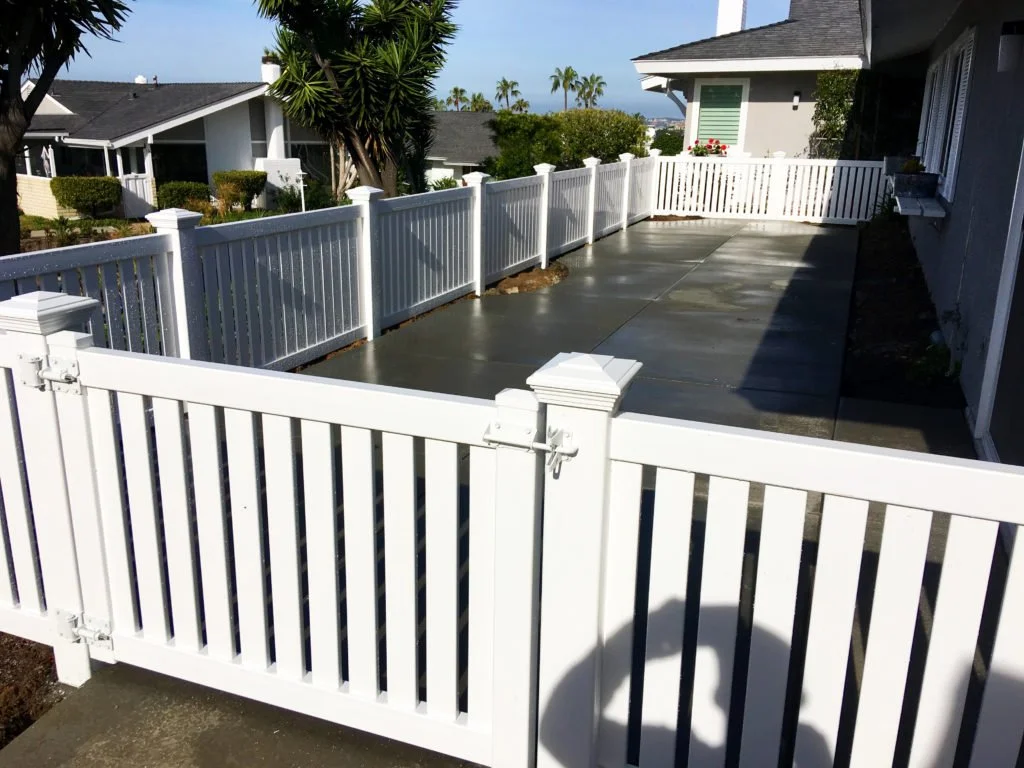 Laguna Niguel outdoor patio with concrete surface and white vinyl railing surrounding the patio, part of a house with siding and windows, with trees and neighboring houses in the background, showcasing vinyl fencing and patio cover potential in Orang