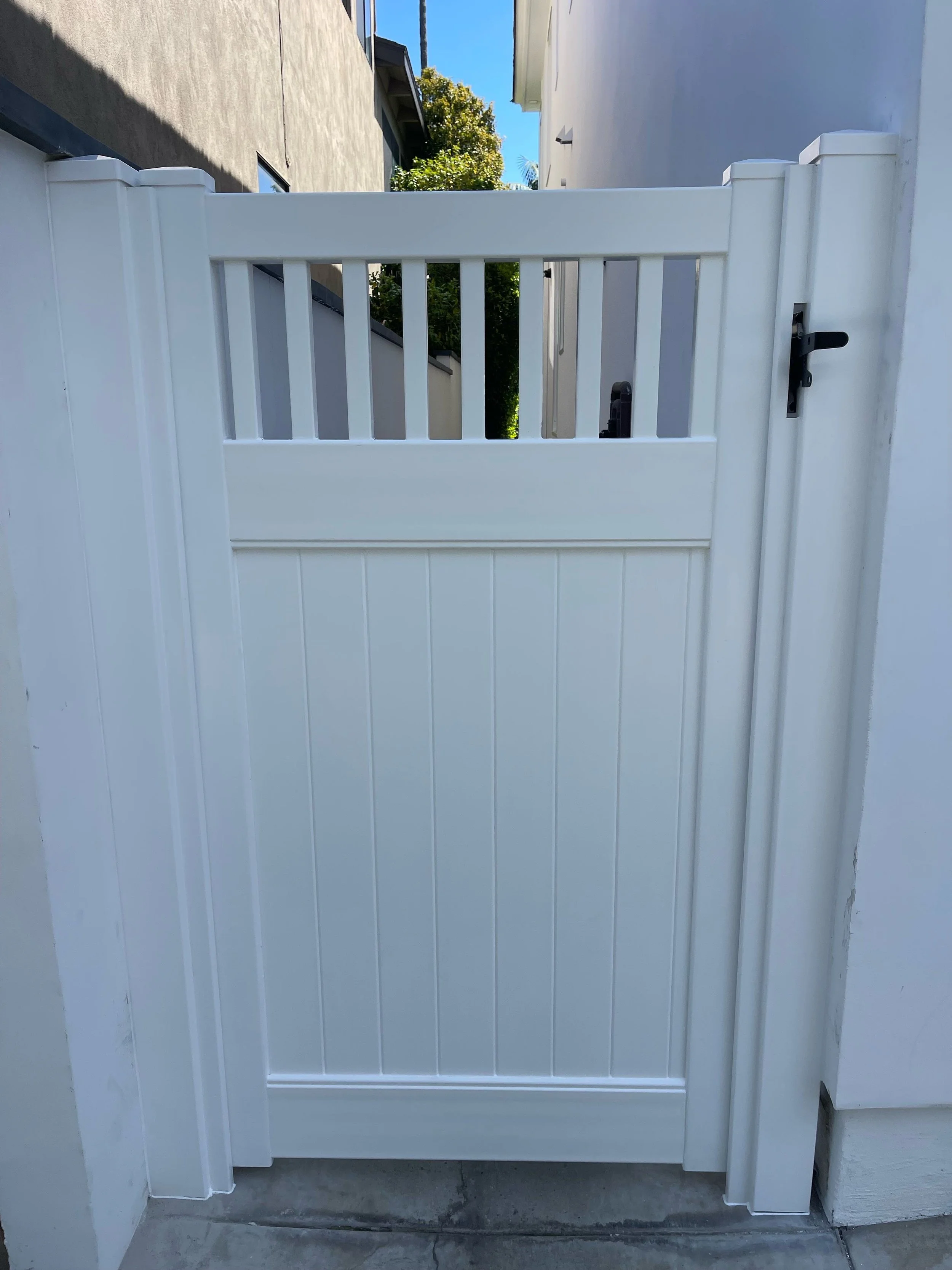 Laguna Beach white vinyl side yard gate with decorative open-top slats and secure latch, framed between stucco walls, modern, low-maintenance fencing solution for coastal Orange County homes.