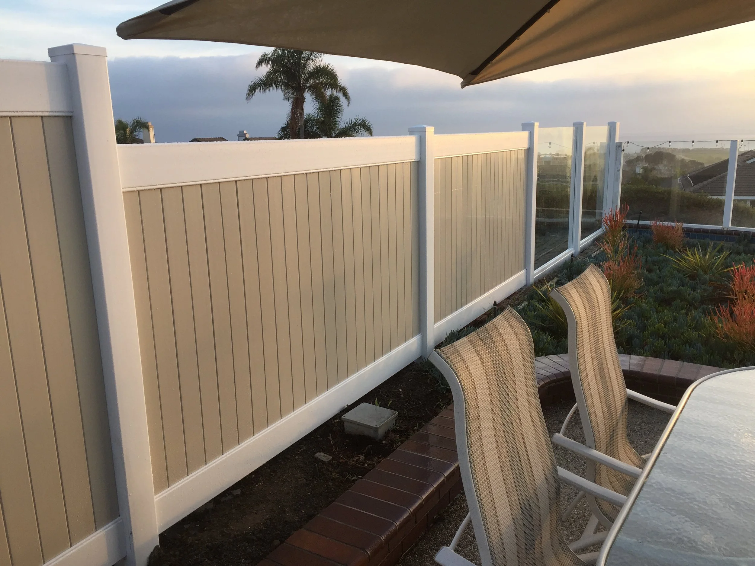 Placentia outdoor patio area with beige chairs and a white fence overlooking a landscape with trees and houses during sunset, exemplifying custom vinyl patio covers and fences.