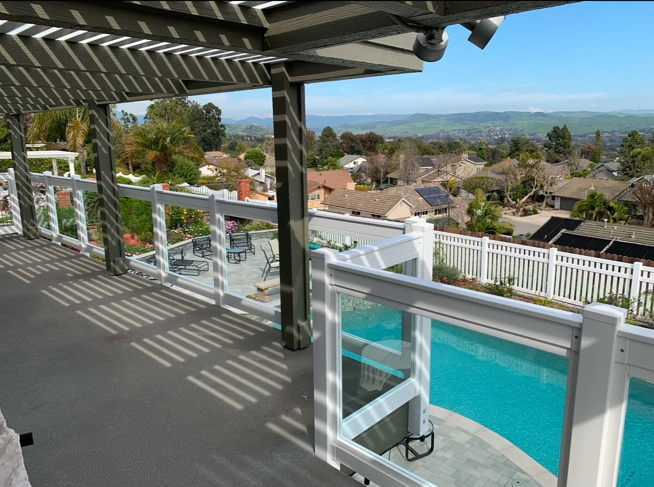 Laguna Beach view from a covered patio with a white railing overlooking a backyard swimming pool and scenic hills in the distance, showcasing attractive vinyl patio covers and fences.