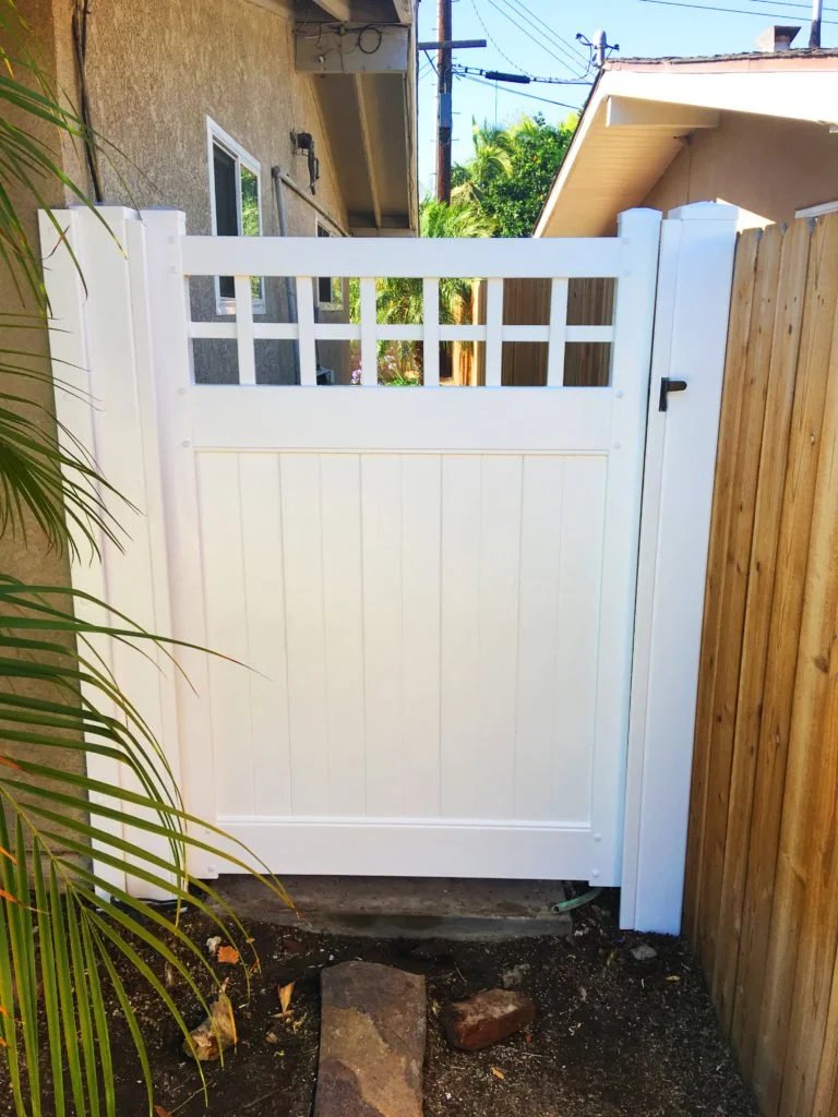 Laguna Hills white vinyl gate installed between a beige stucco wall and a wooden fence in a backyard with stepping stones, demonstrating how vinyl gates enhance privacy and durability for Orange County homes.