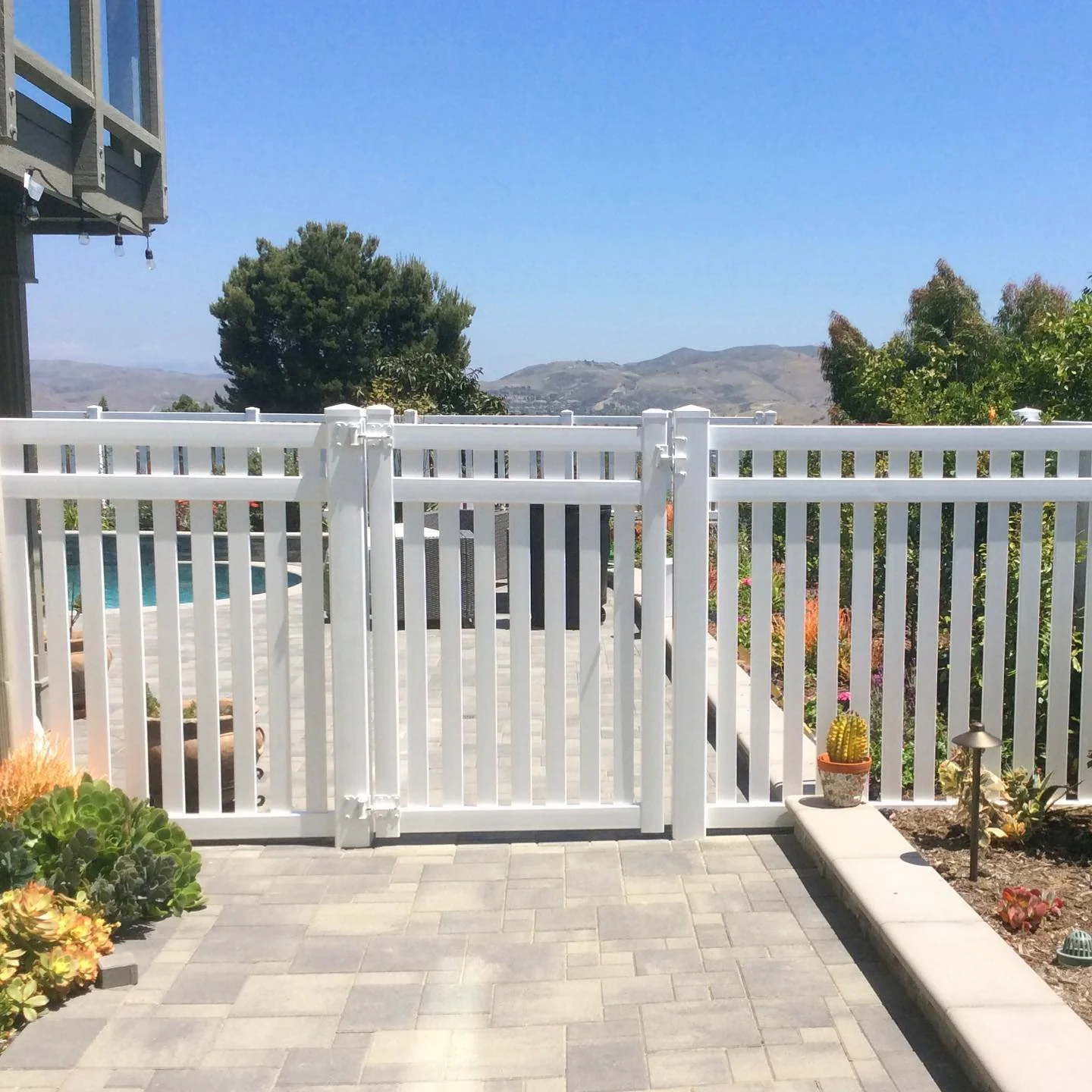 La Palma patio view with white vinyl fence and gate, potted cactus and colorful flowers overlooking rolling hills and distant mountains under clear blue sky, showcasing beautiful outdoor living with vinyl fences in Orange County.