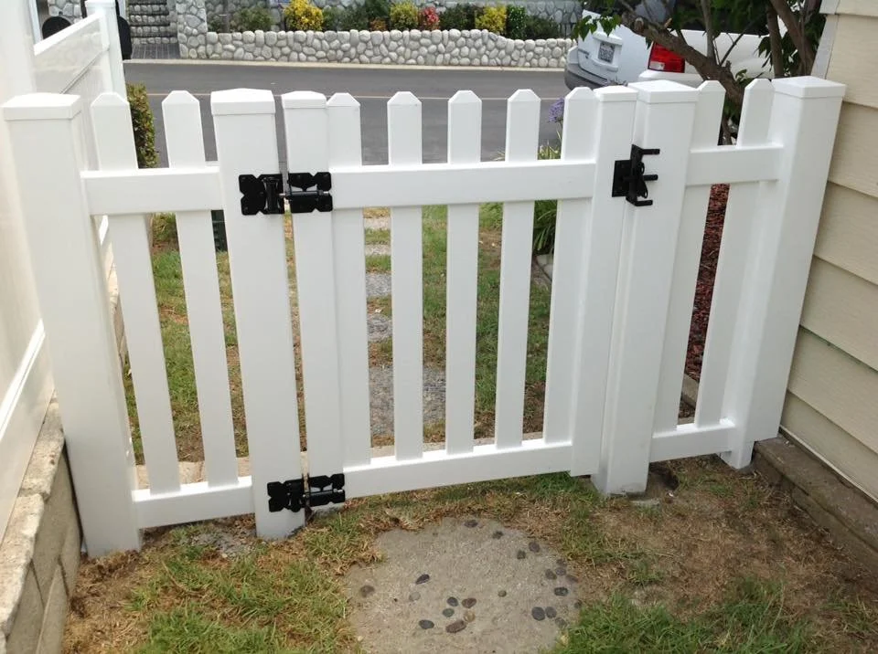Seal Beach white vinyl picket gate with black hinges and latch leading to a sidewalk and residential street, showcasing durable vinyl fencing and custom gates in Orange County.