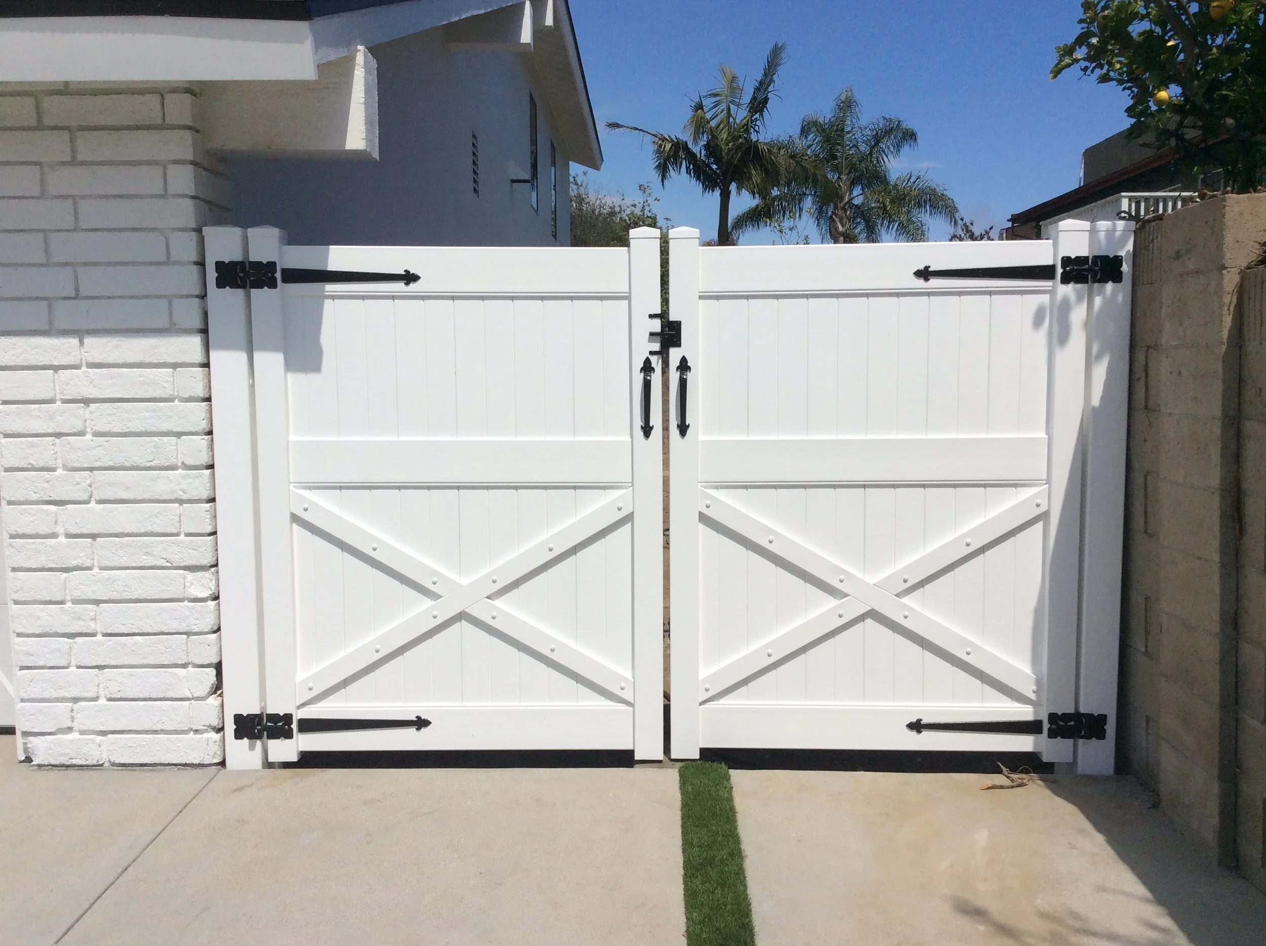 Mission Viejo white vinyl ranch-style double gate with decorative crossbuck “X” panels and black hardware, installed between a block wall and white brick home, classic, durable driveway entry for Orange County residences.