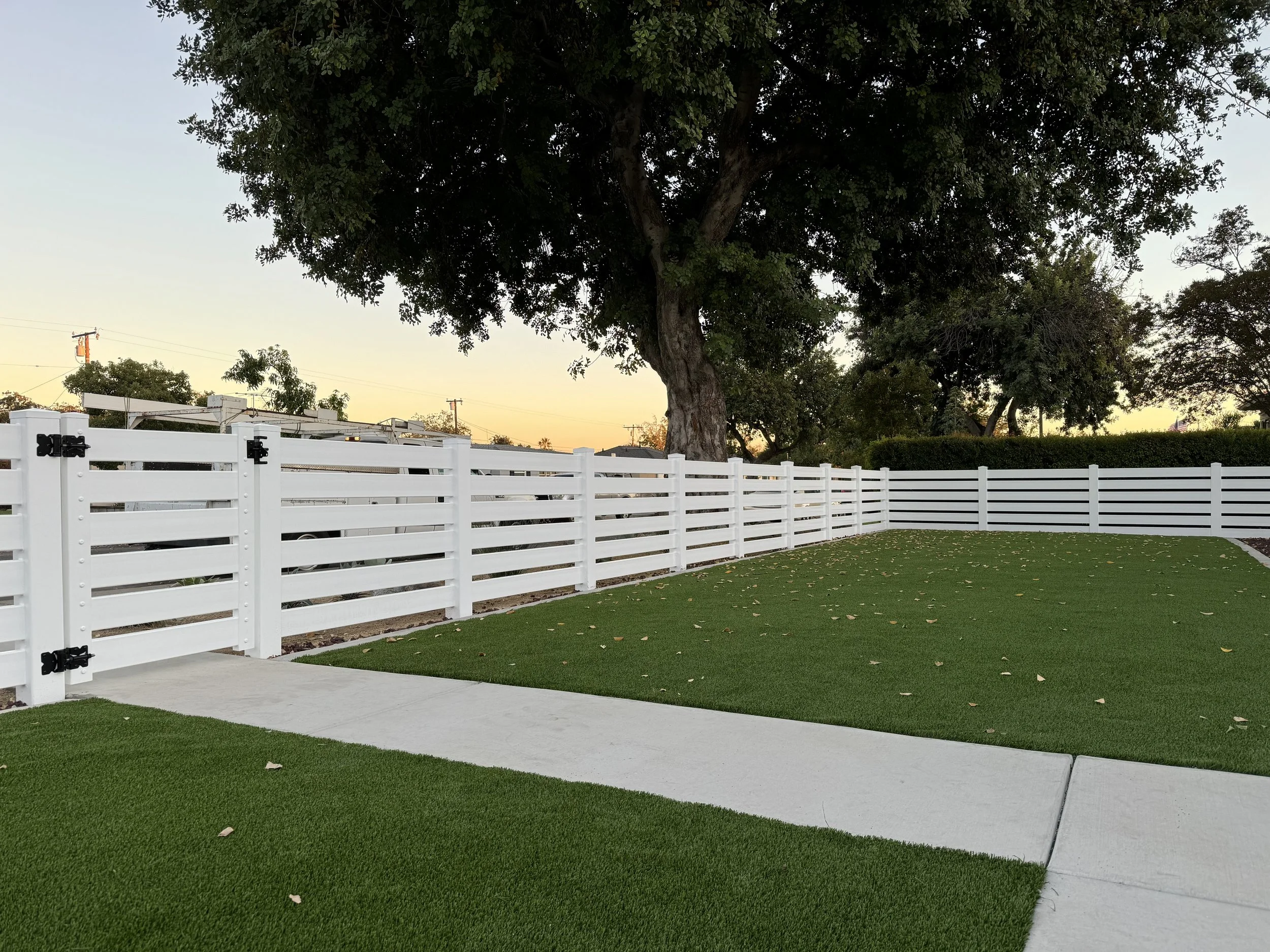 Costa Mesa horizontal white vinyl ranch-style fence with matching gate, enclosing a backyard with artificial turf and concrete walkway, modern, durable fencing option for Orange County properties.