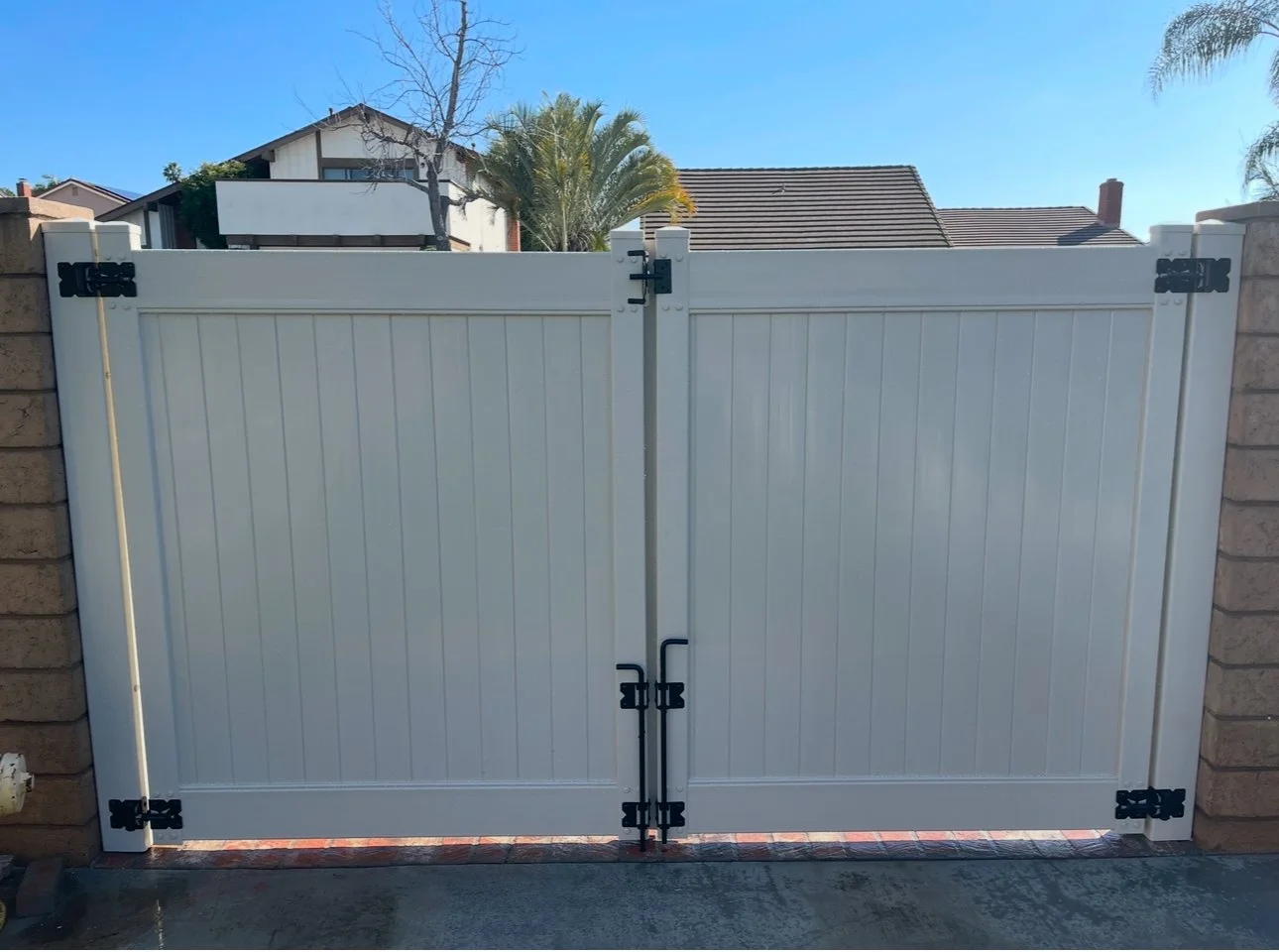Huntington Beach white vinyl double driveway gate with black hardware, installed between block walls, providing full privacy and secure access for Orange County homes.