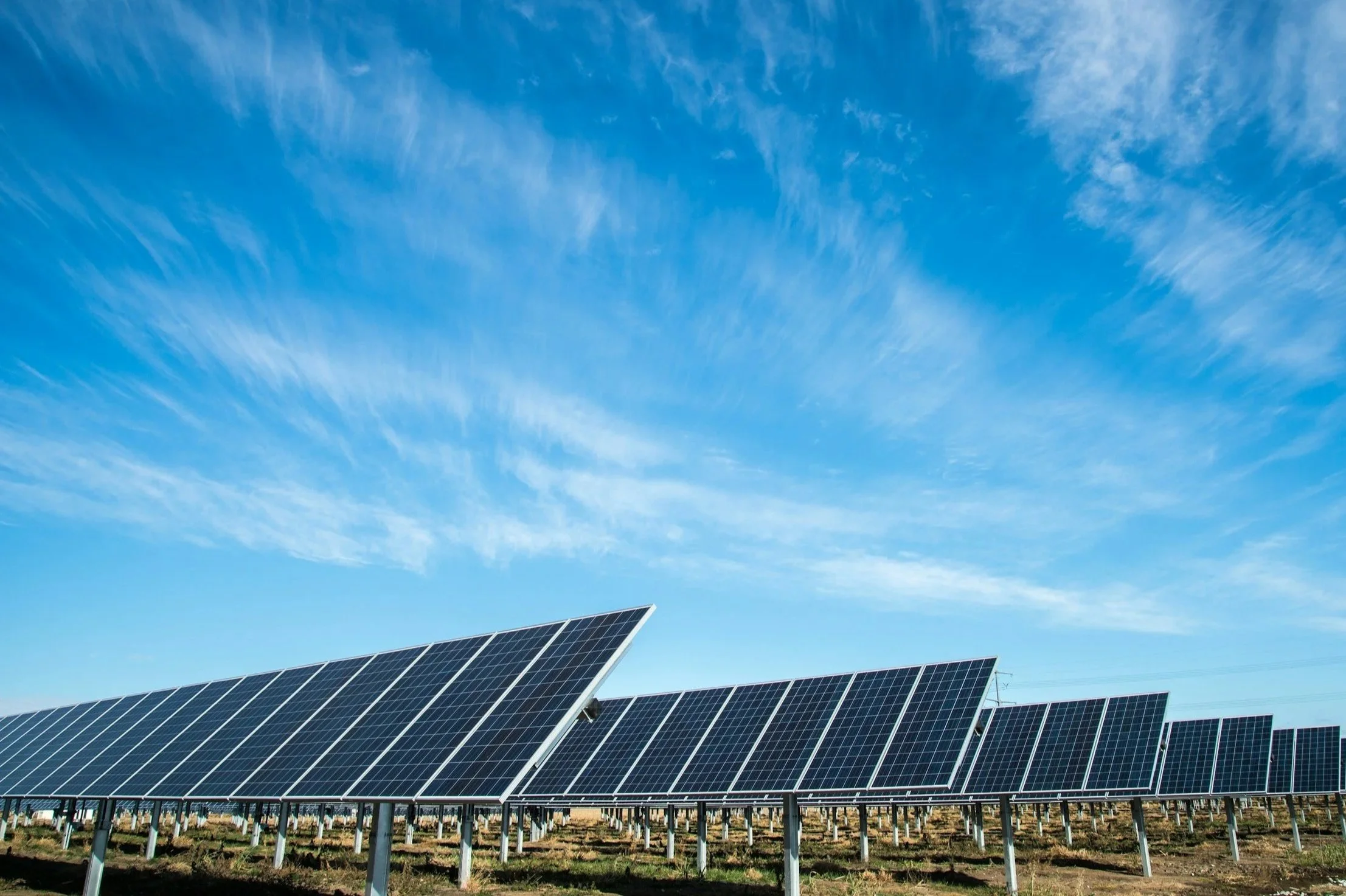 Solar panels in a field under a bright blue sky with scattered clouds.