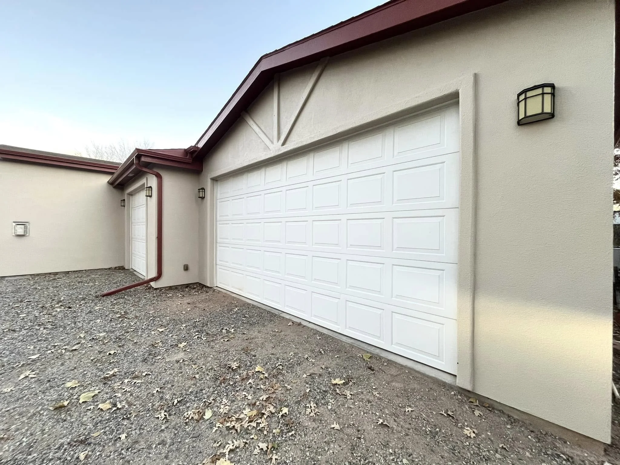 Exterior view of a house with a white garage door, beige walls, red roof, and outdoor lighting fixtures.