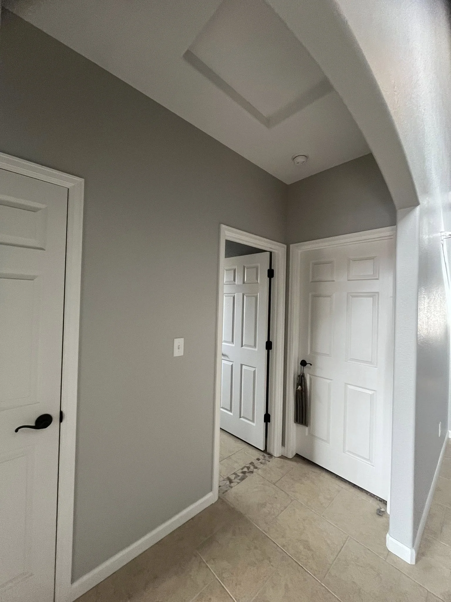View of an interior hallway with gray walls, white doors, tiled flooring, and a rounded archway on the right side.