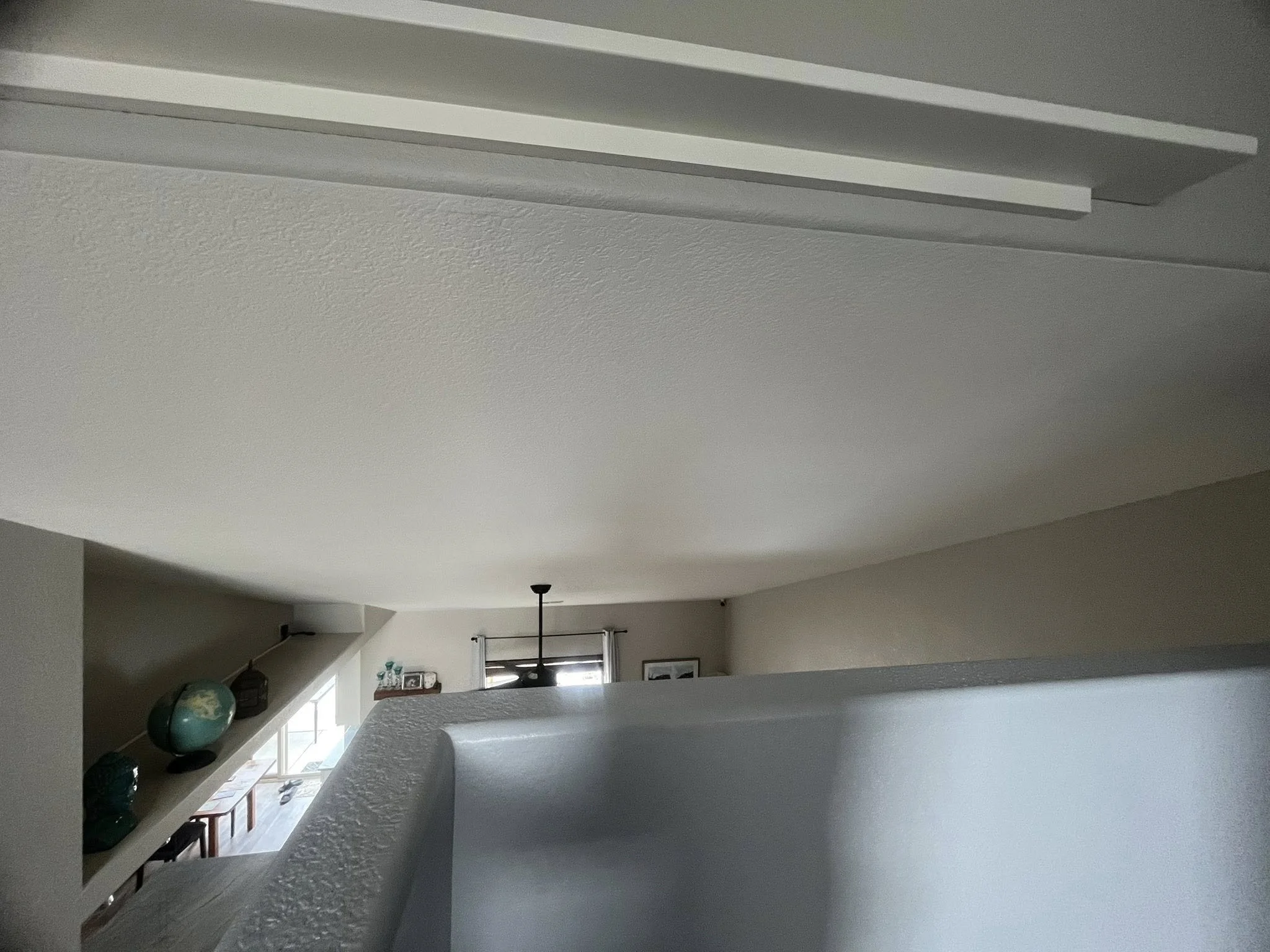 Interior view of a modern home with a view of the living area, angled ceiling, window with curtains, and decorative items on the shelves.