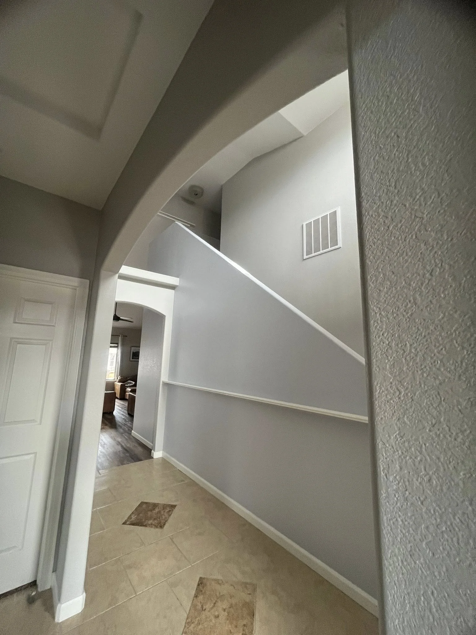 Interior view of a home's entryway with tiled floor, white walls, and a staircase leading upstairs.