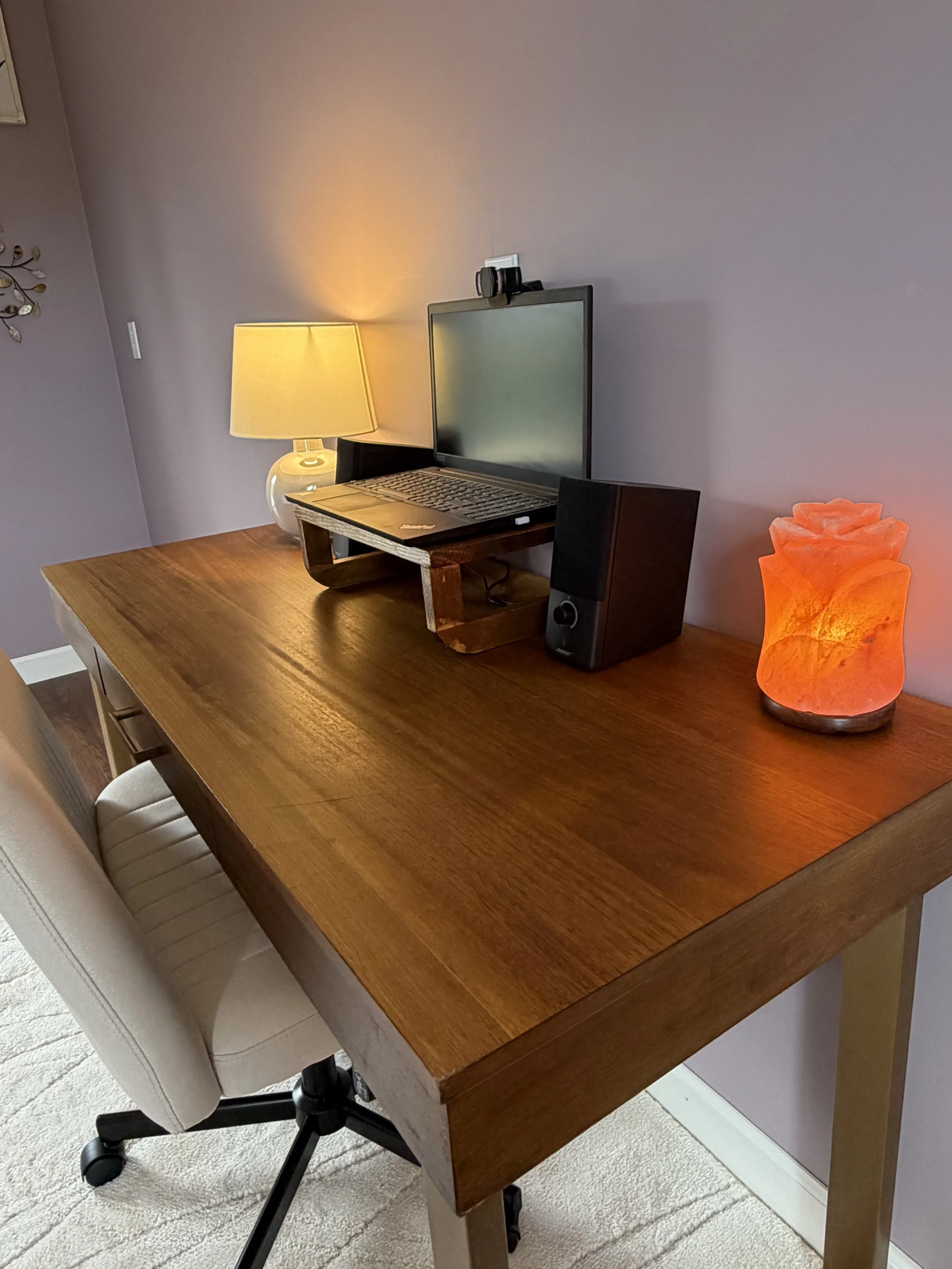 Warm, private telehealth workspace with a wooden desk, laptop, and soft lighting.