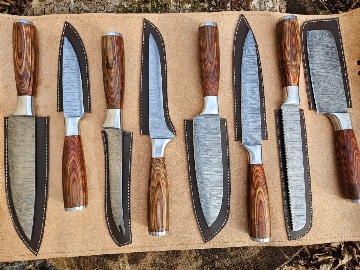 A collection of eight chef knives with Damascus steel blades and wooden handles, displayed on a leather mat with individual knife sheaths.