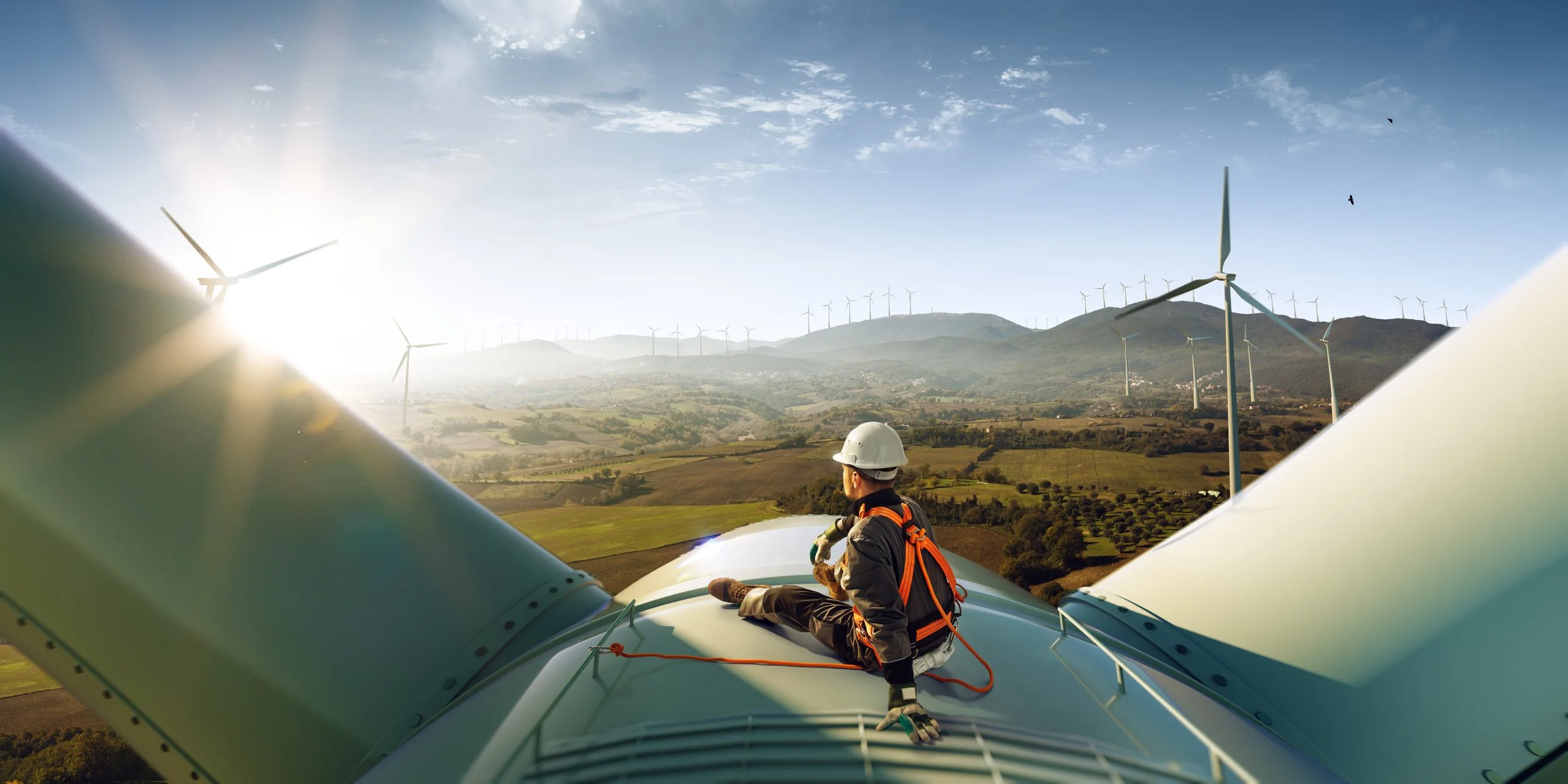 An engineer sitting on a modern windmill, looking out at a field of windmills
