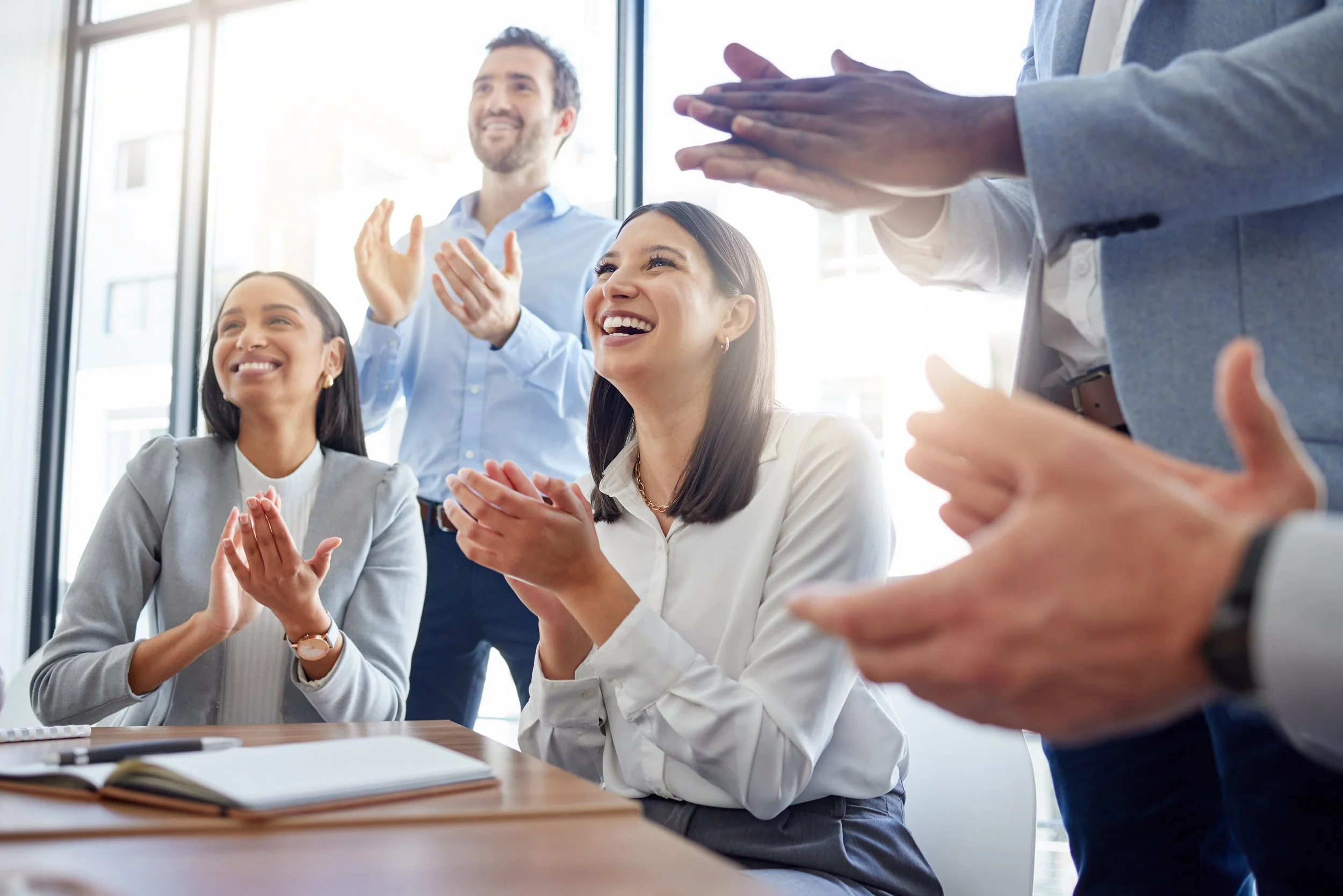 A group of business women and men clapping and cheering at a meeting