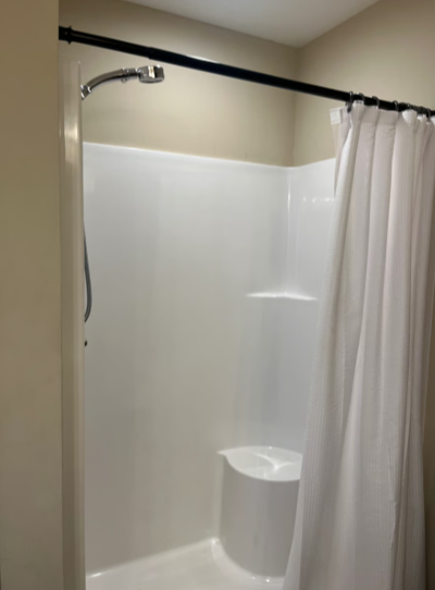 A simple shower area with a white shower curtain, a showerhead, and a built-in soap dish in a bathroom corner.