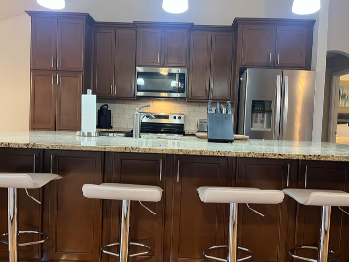 Modern kitchen with wooden cabinets, stainless steel appliances, a granite countertop, and white barstools.