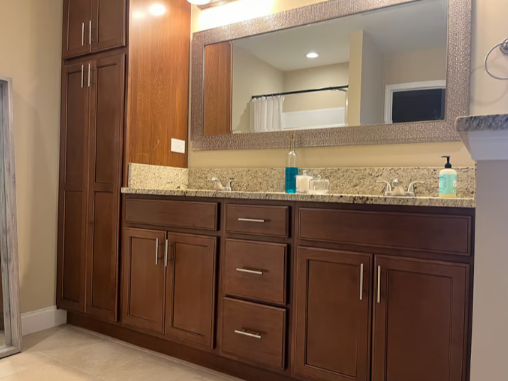 Bathroom vanity with brown cabinets, a large mirror, soap dispenser, hand sanitizer, and a bottle of blue liquid soap.