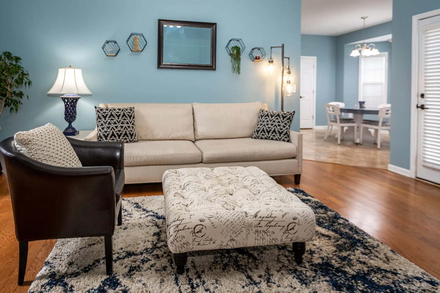 Living room with beige sofa, black armchair, patterned ottoman, and blue walls