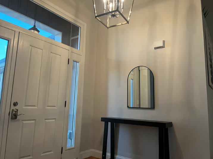 Entryway with a white front door, a tall narrow window beside it, a black console table, an arched mirror above the table, and a modern chandelier hanging from the ceiling.