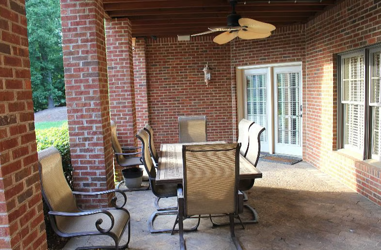 Covered outdoor patio with a brick wall, a dining table, six chairs, a ceiling fan, and a door leading outside.