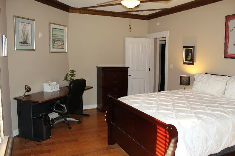 A bedroom with a wooden bed, desk, office chair, dresser, and framed wall art.