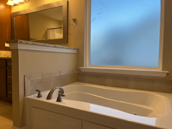 Bathroom with a bathtub next to a frosted window, a mirror, and a granite countertop.